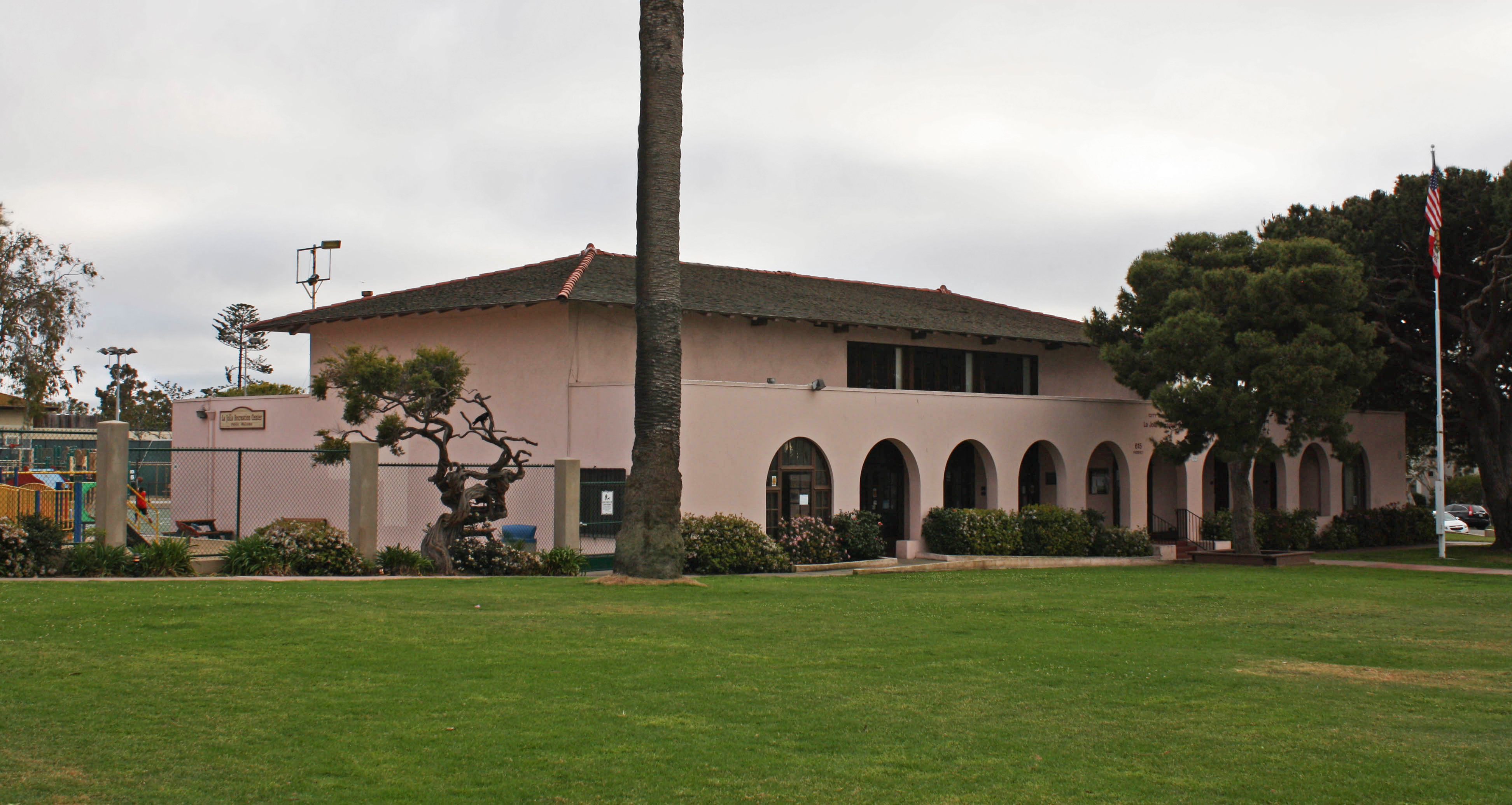 Pink single-story building with arched entryways, a tall palm tree, and an American flag.