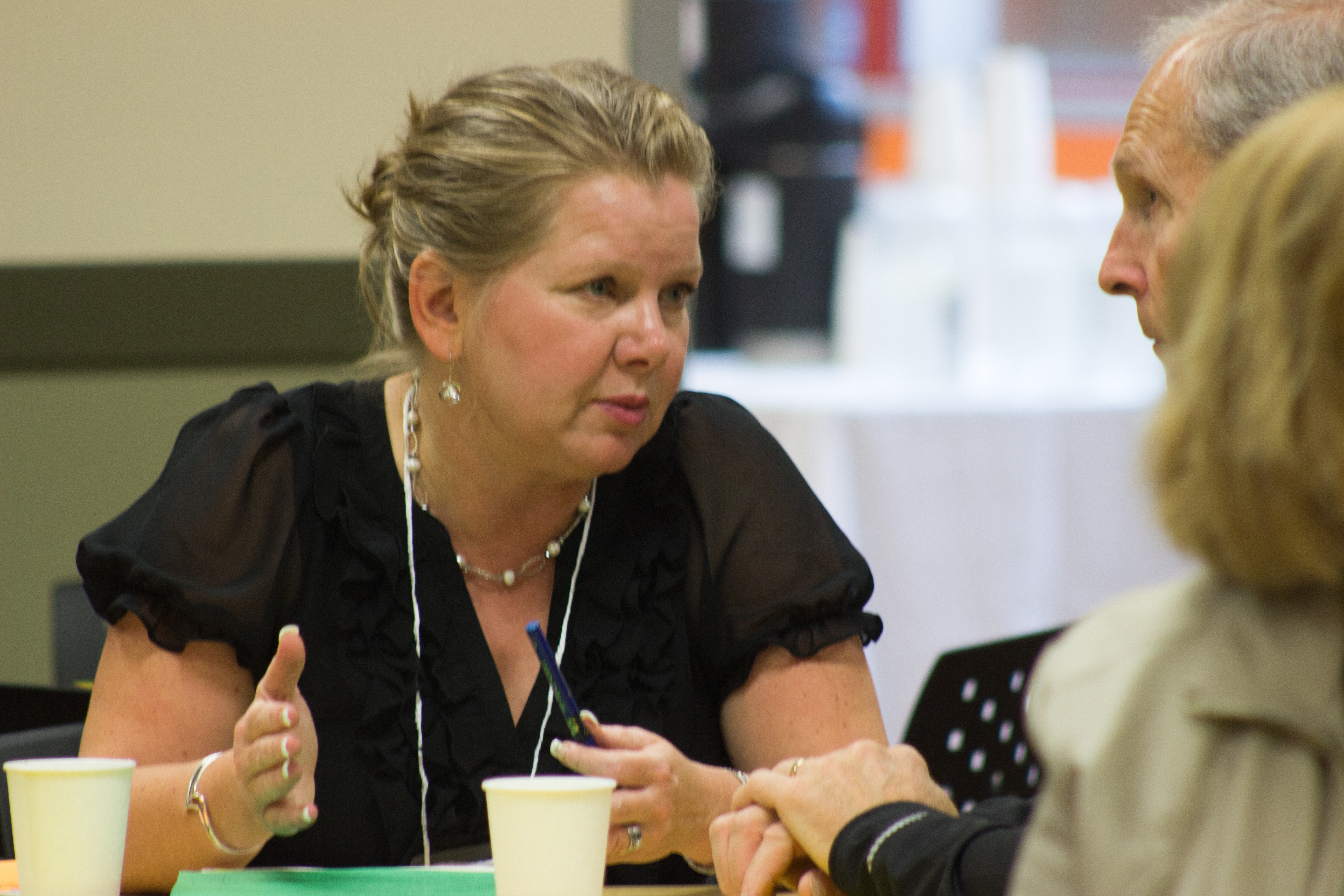 A woman gestures while speaking to a man seated across a table at a workshop.