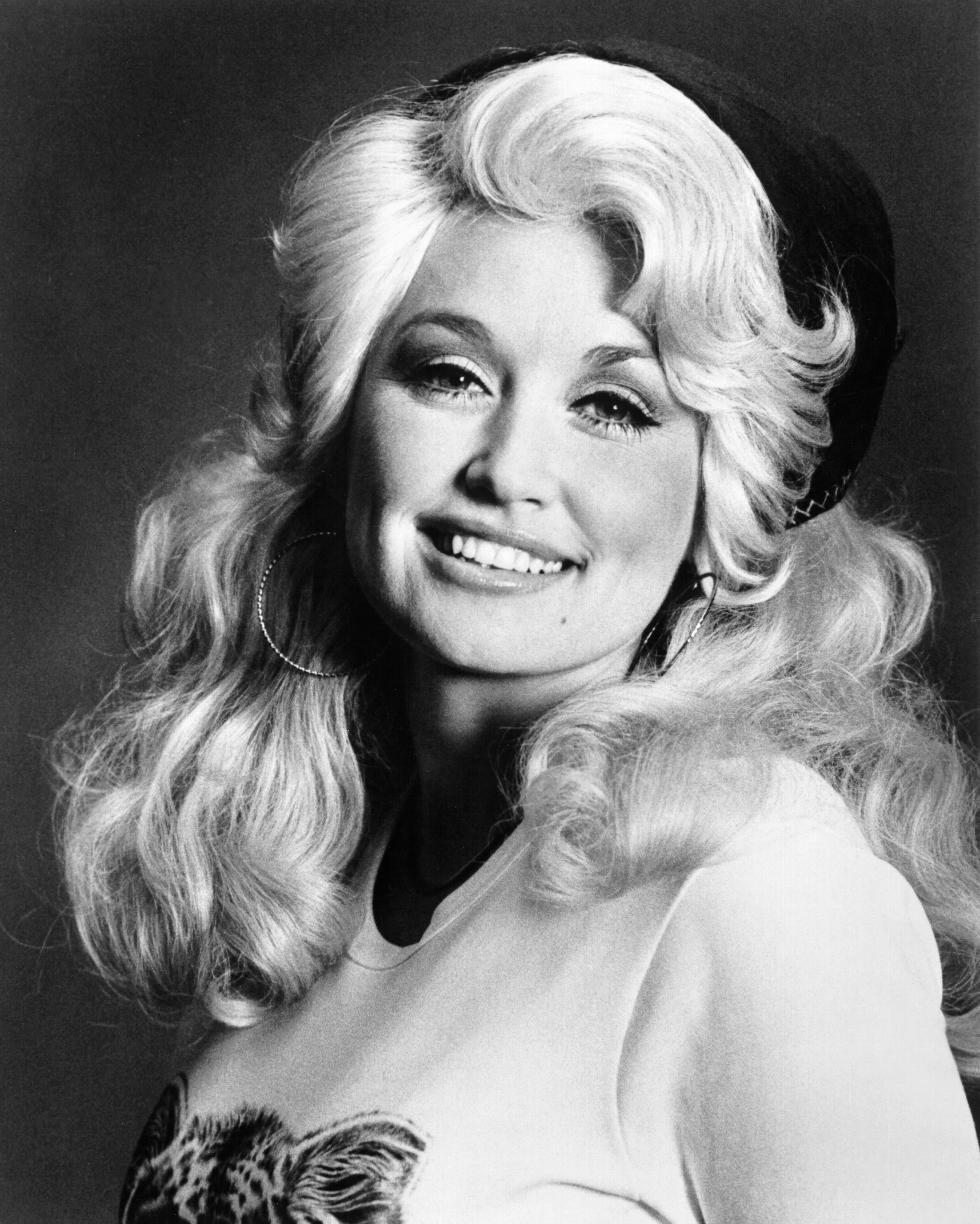 Black-and-white portrait of a smiling woman with large styled blonde hair.