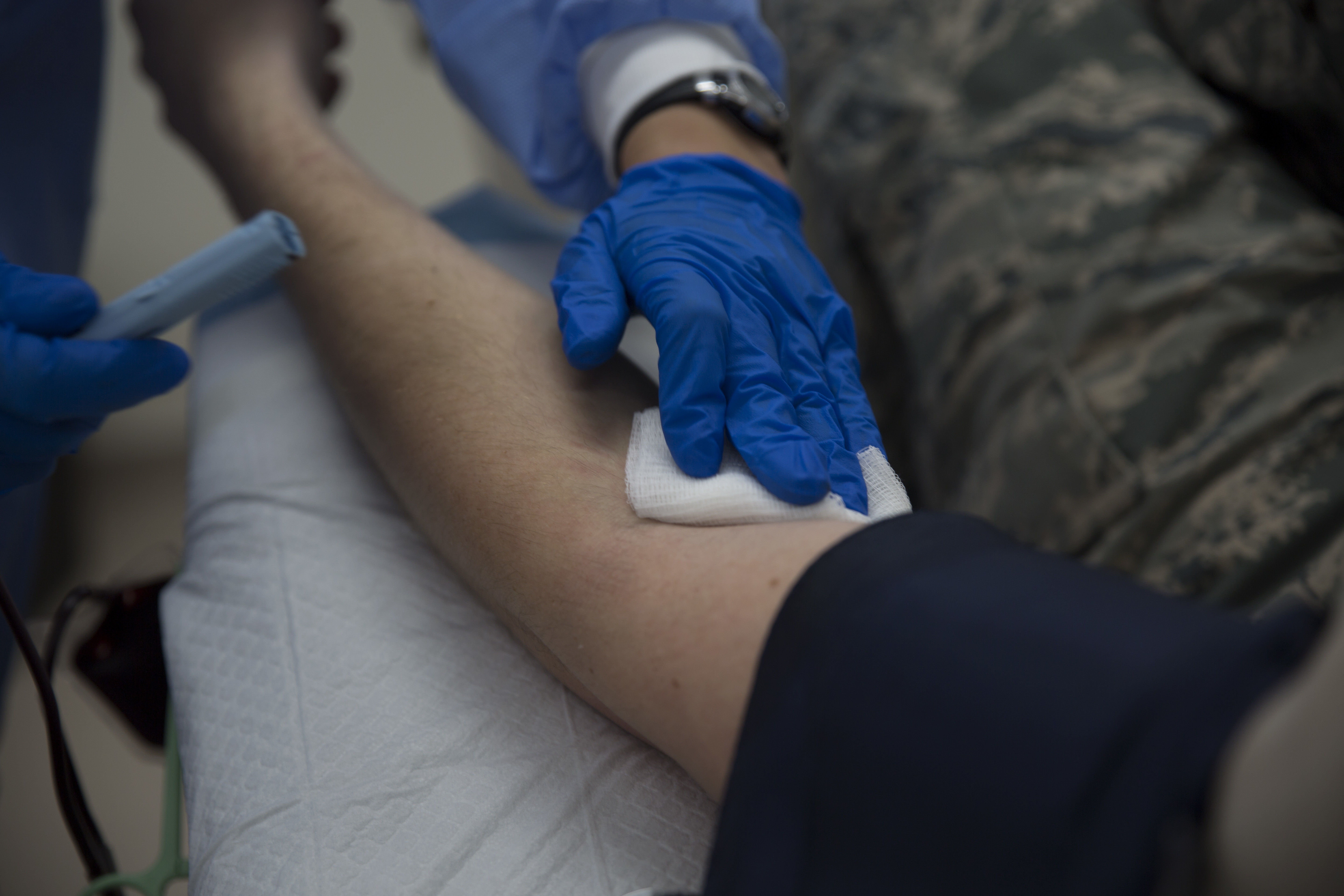 Gloved technician pressing gauze on a donor's inner arm after a blood draw.
