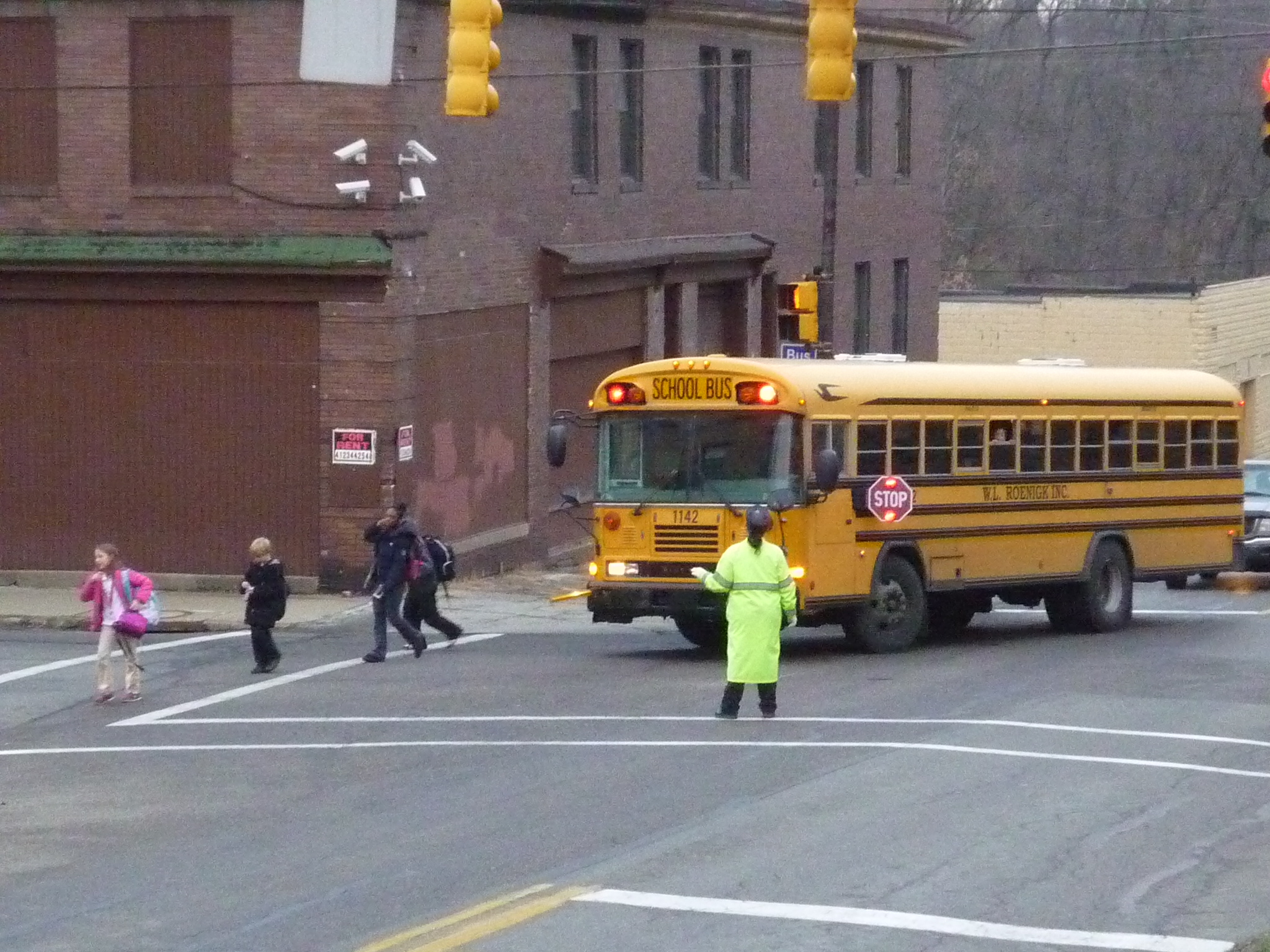 Crossing guard in yellow vest directs traffic at an intersection as children cross.