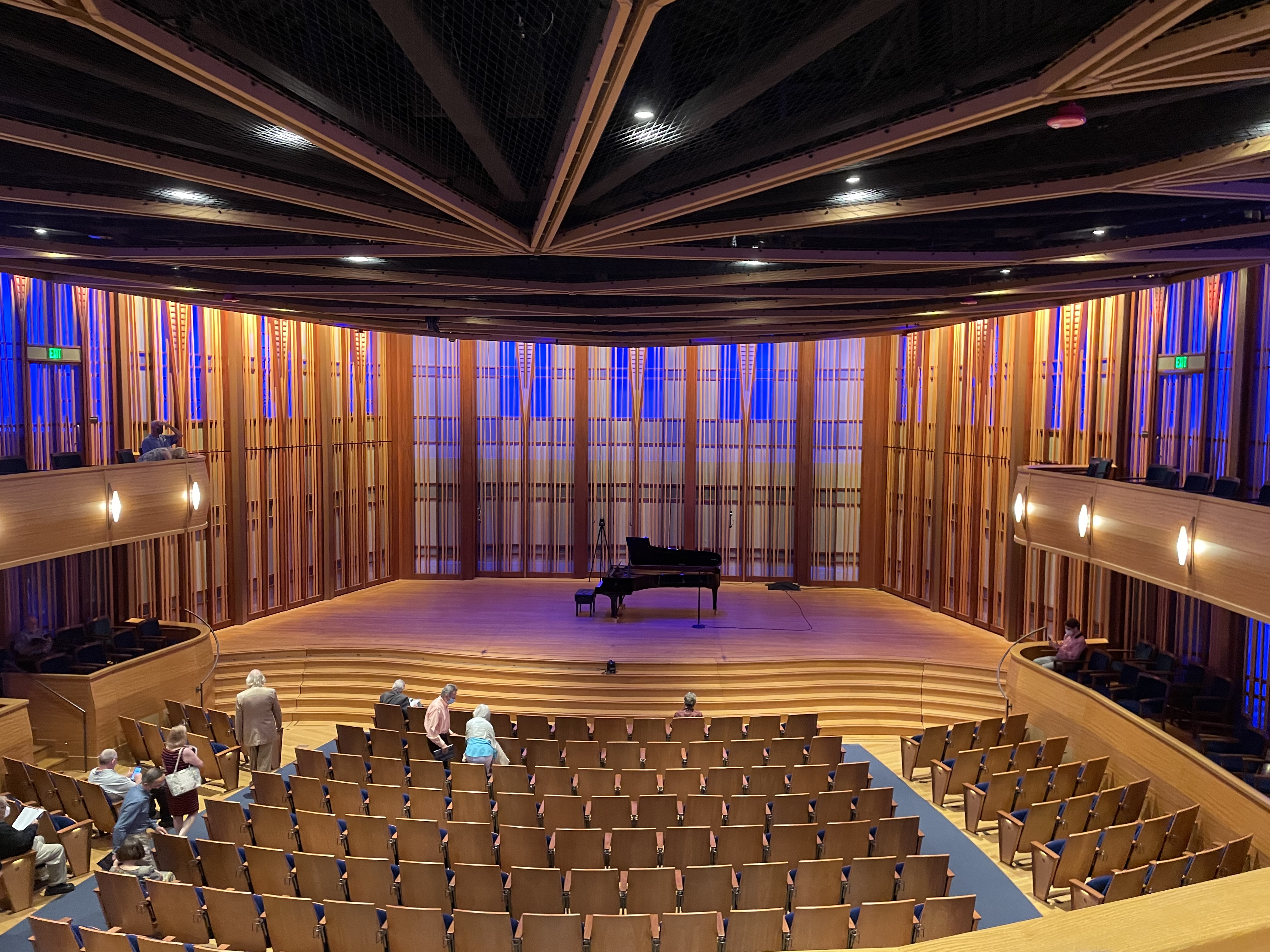 Empty concert hall interior with tiered wooden seating and a grand piano on stage.