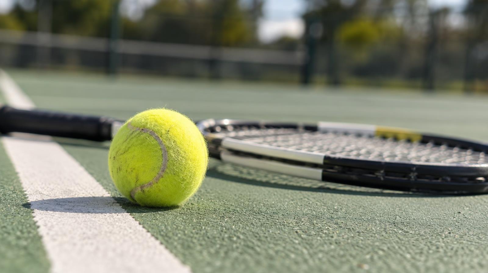 Yellow tennis ball and racket resting on a green outdoor hard court.