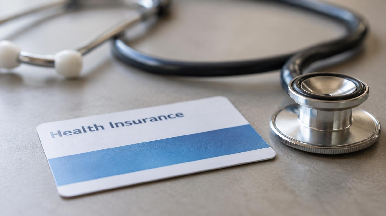 A health insurance card and stethoscope resting on a plain surface.