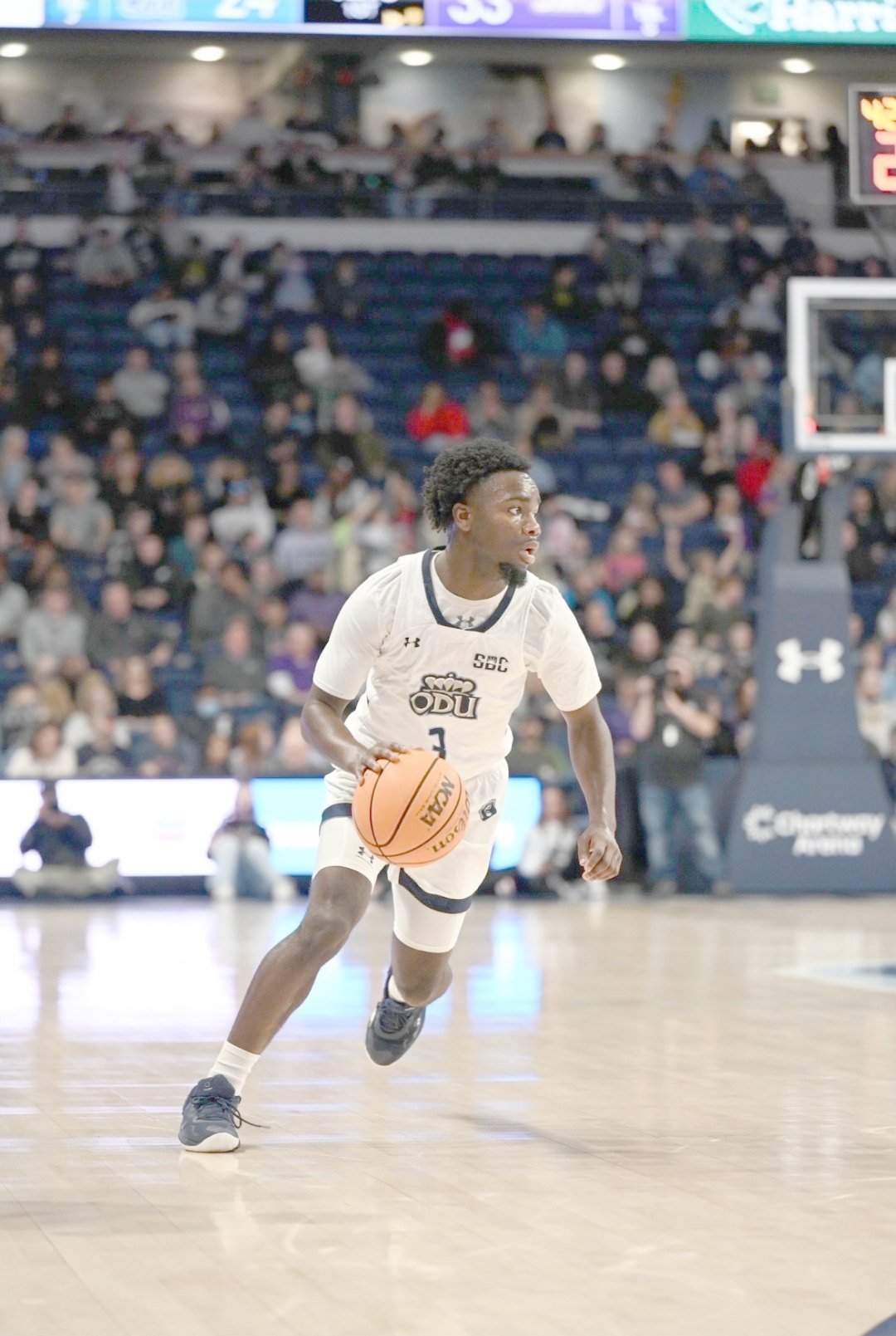 Basketball player in white ODU jersey number 1 dribbles on an indoor court.