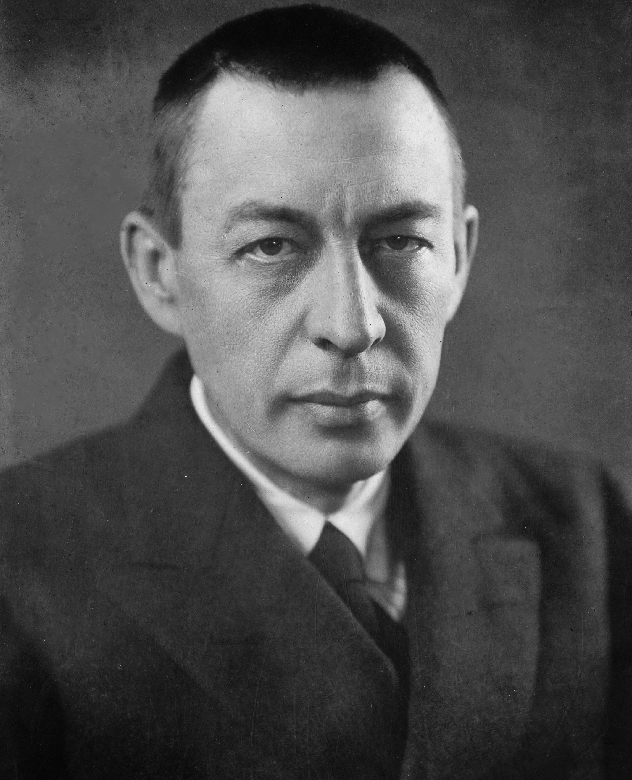 Black-and-white portrait of a man in a dark suit and tie, looking directly at the camera.