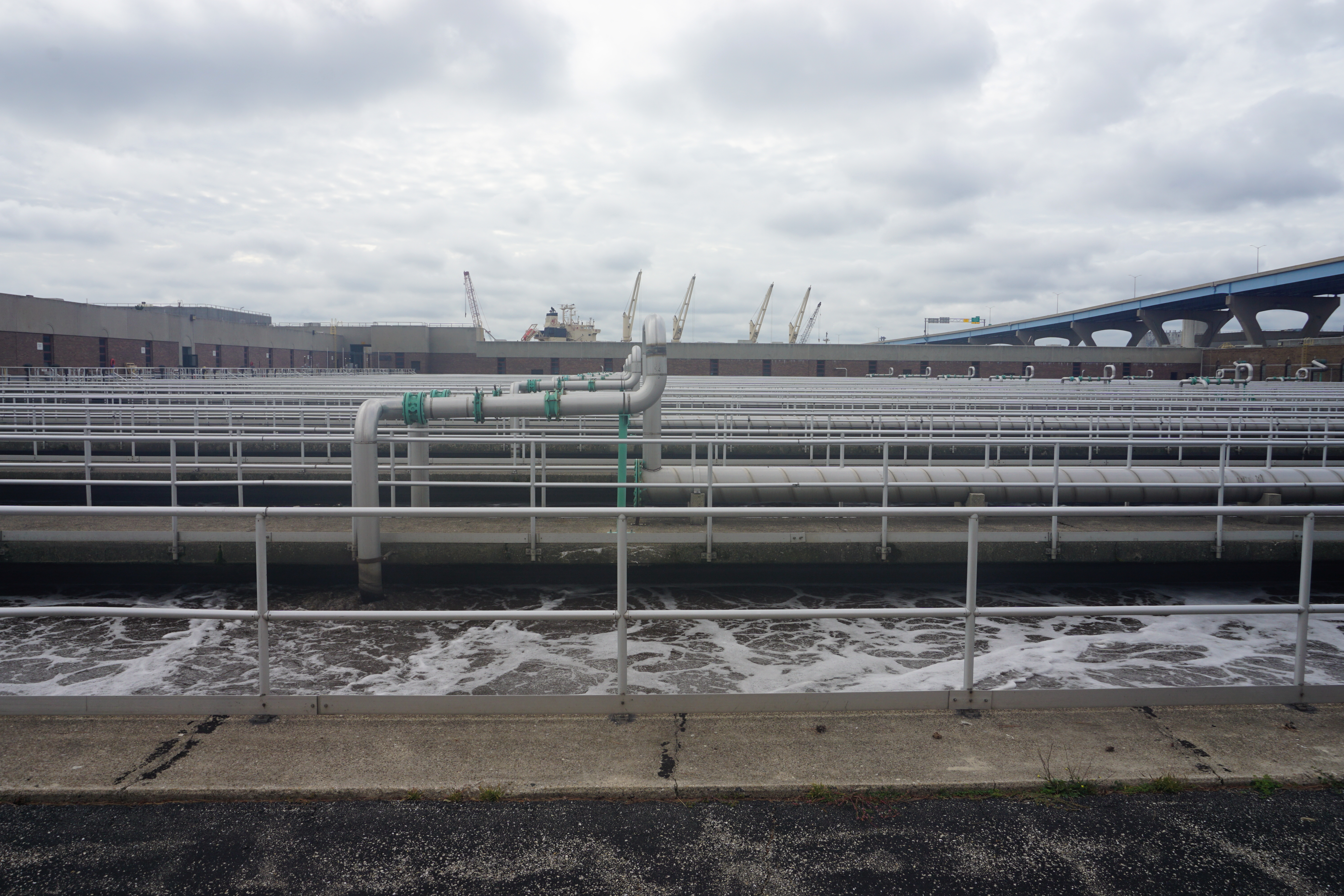Parallel outdoor water treatment basins with white railings and green pipes at an industrial facility.