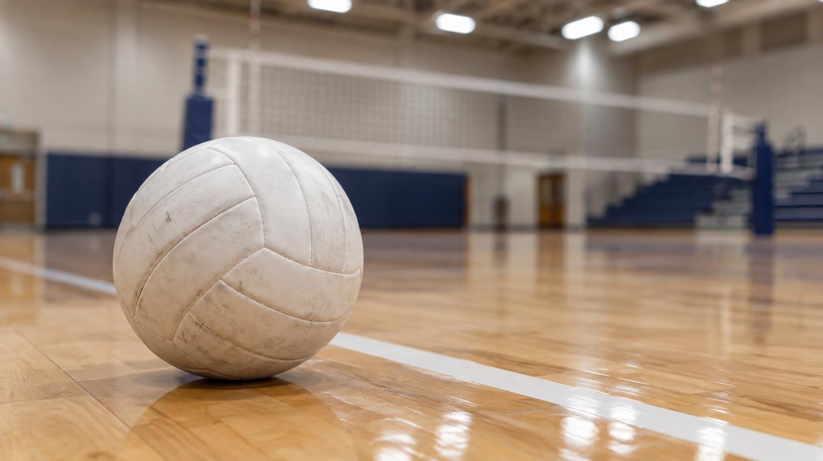 White volleyball resting on a hardwood gym floor near a painted boundary line.