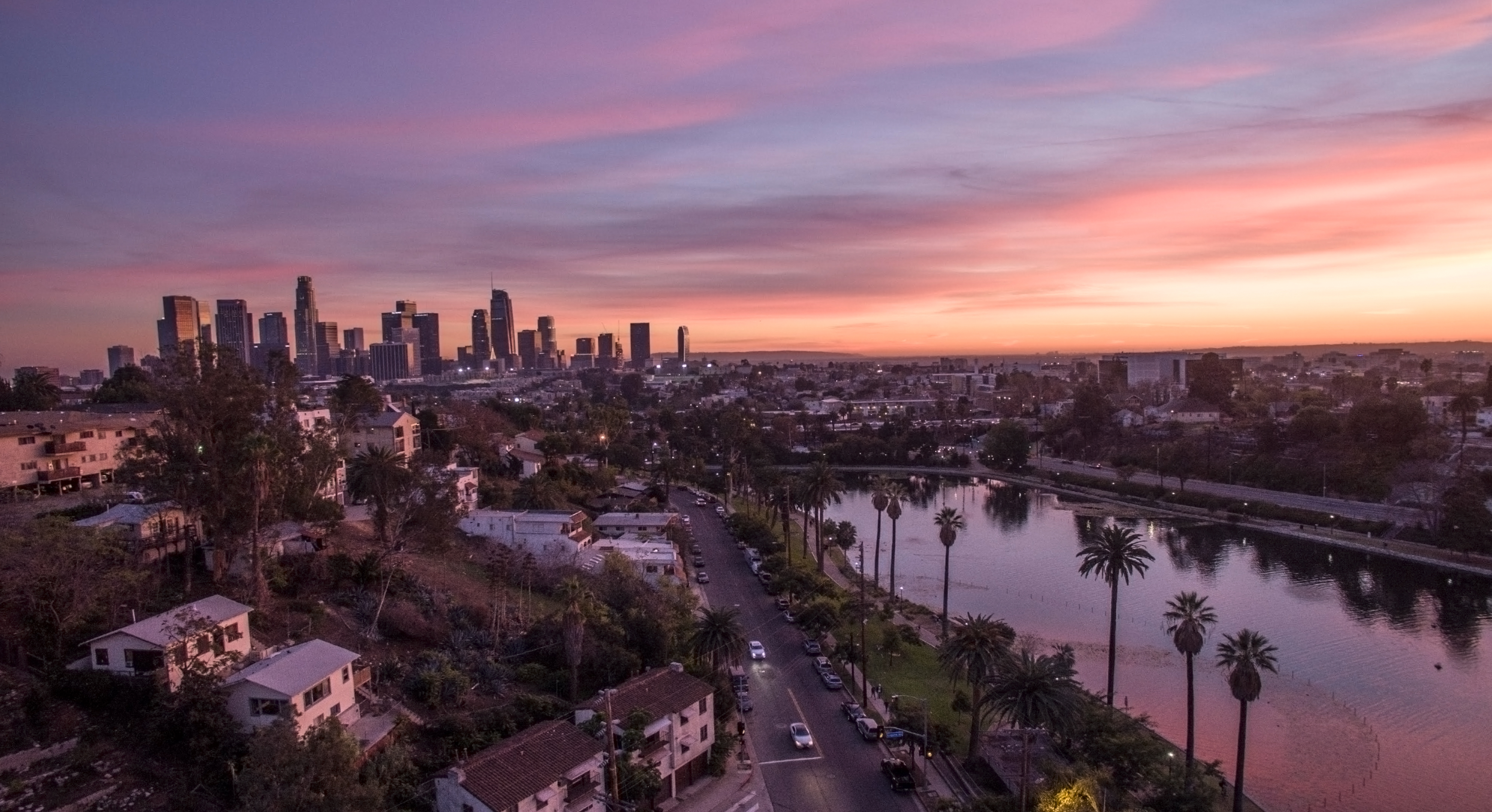 Aerial view of Echo Park Lake with palm trees and the Los Angeles skyline at sunset.