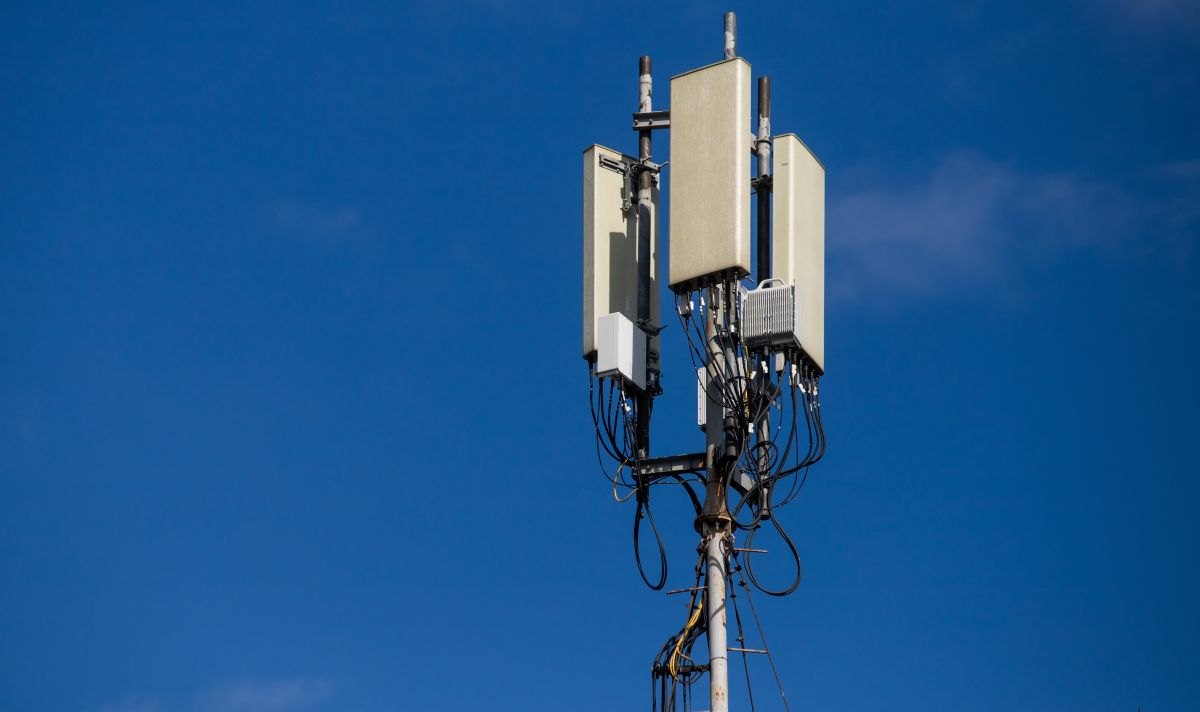 A cellular monopole tower with panel antennas mounted at the top against a clear blue sky.