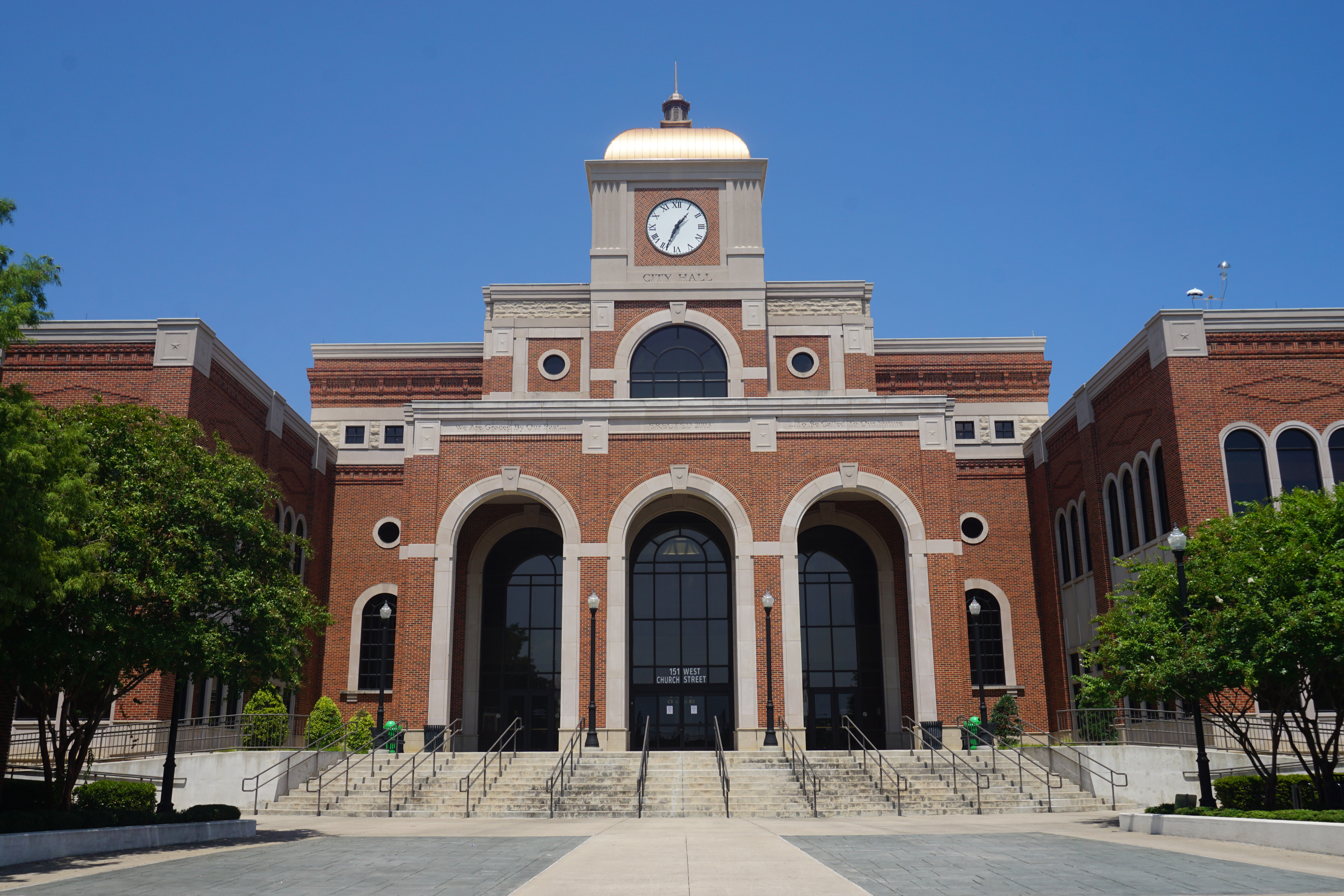 Red-brick city hall building with arched entryways and a gold-domed clock tower.