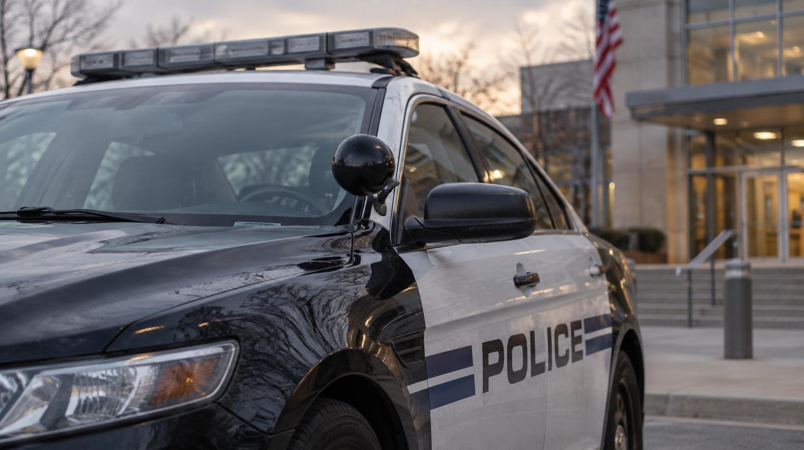 A police patrol car with an unlit light bar parked outside a building at dawn.
