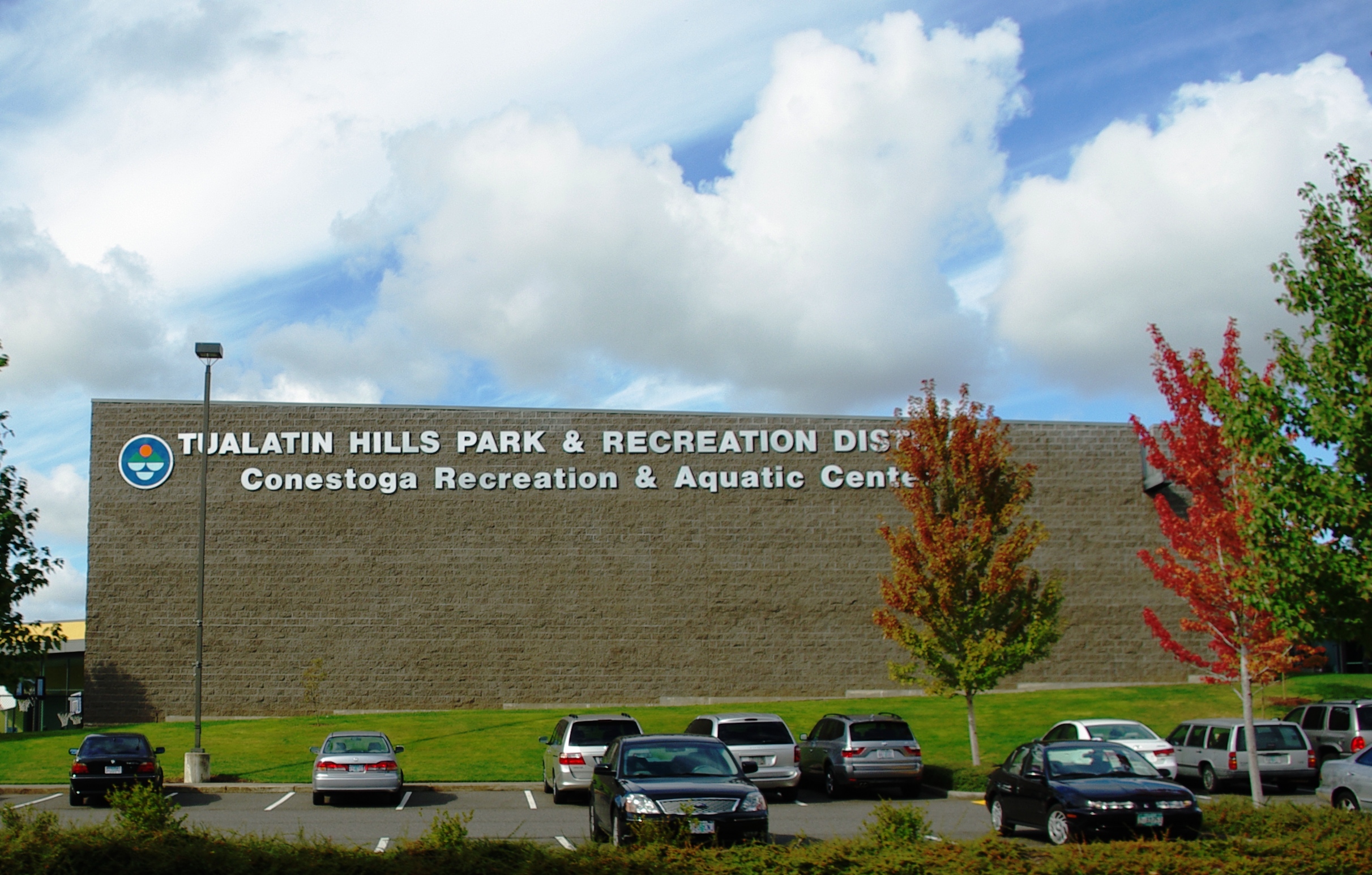 Exterior of a large tan brick recreation center with district signage and a parking lot.