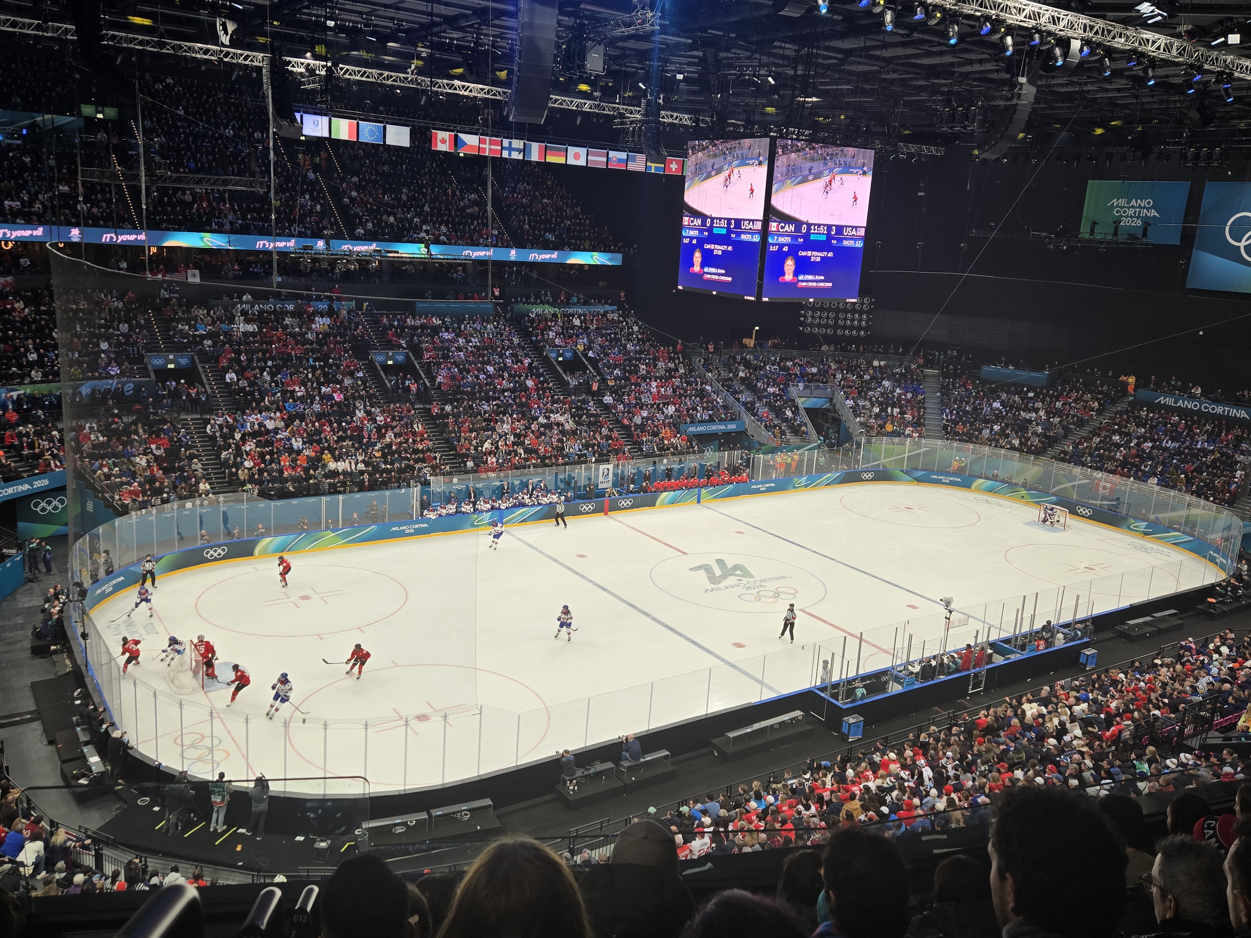 Players from the USA and Canada compete on ice in a packed Olympic hockey arena.