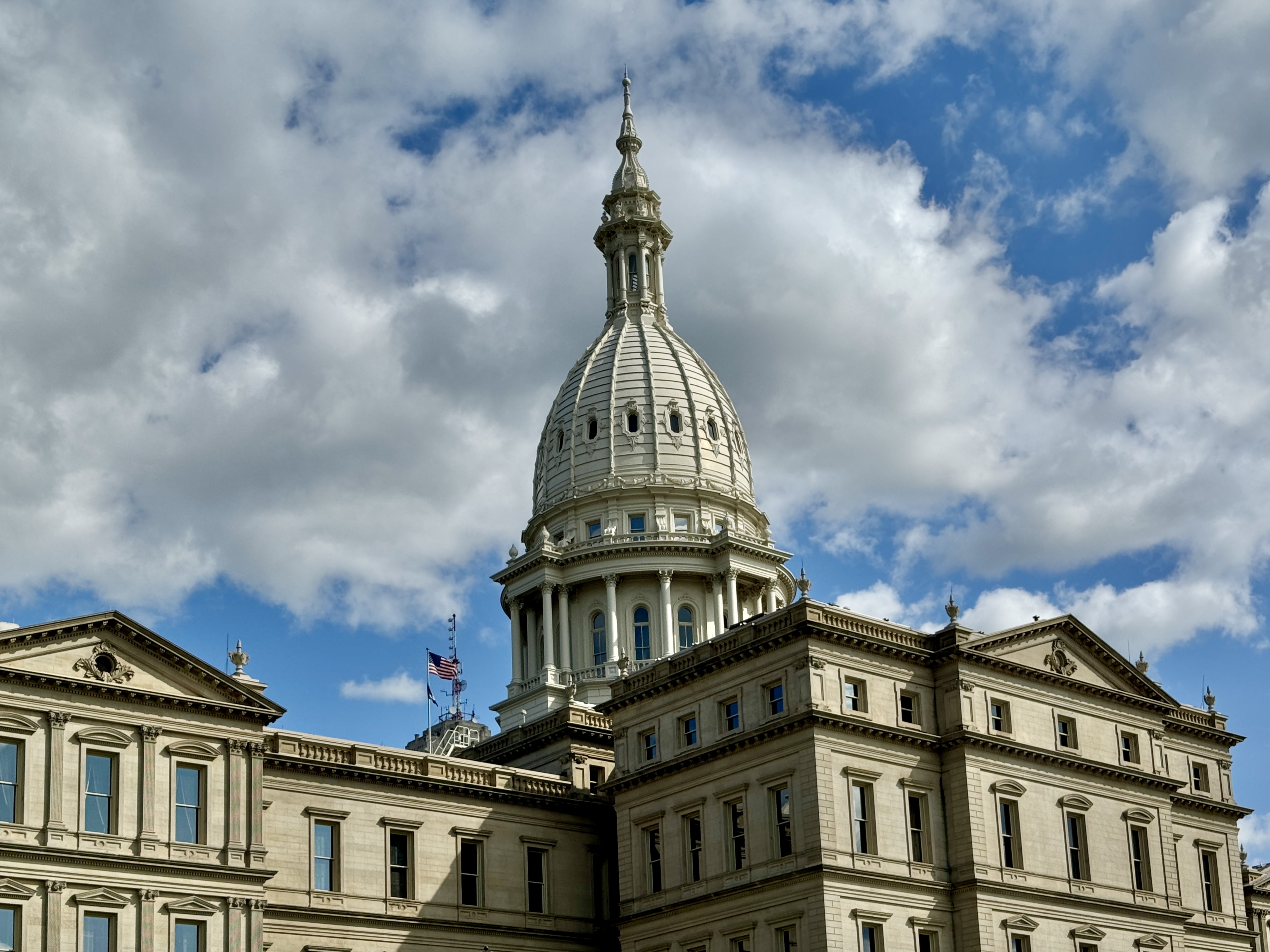 Limestone dome of the Michigan State Capitol building against a partly cloudy blue sky.
