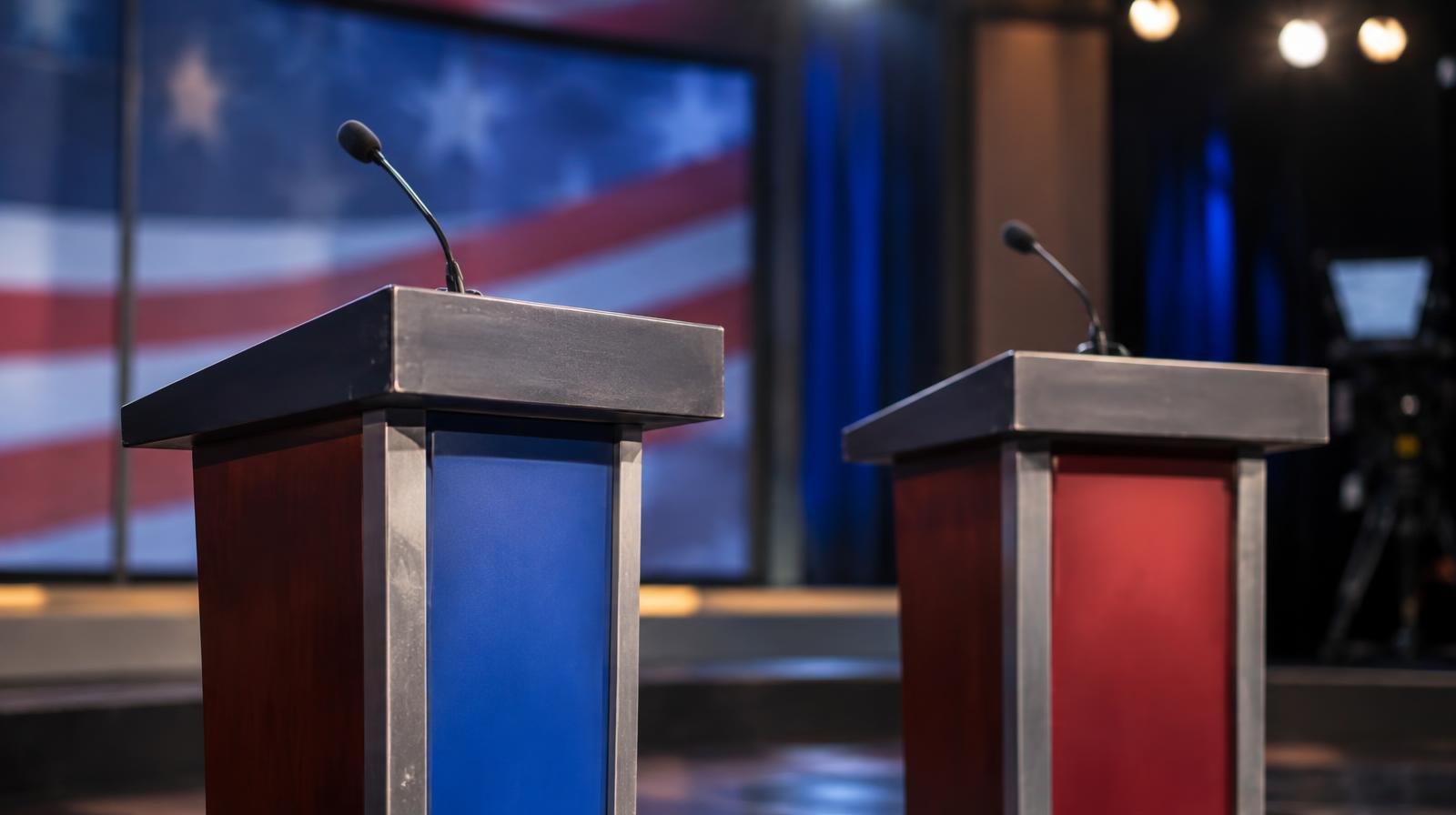 Two empty podiums with microphones on a stage under bright studio lights.