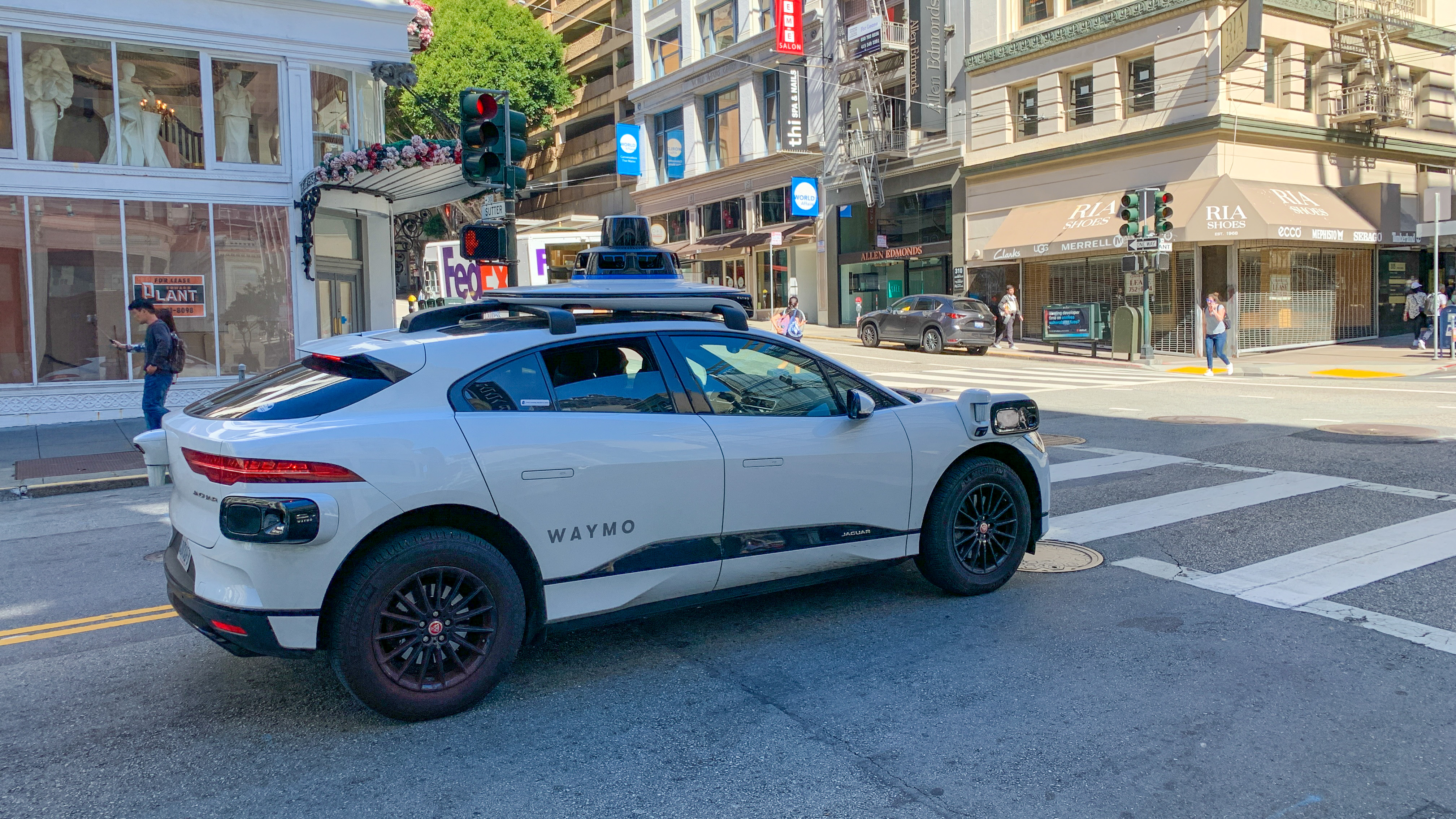 White Waymo self-driving car with roof sensors stopped at an urban intersection.