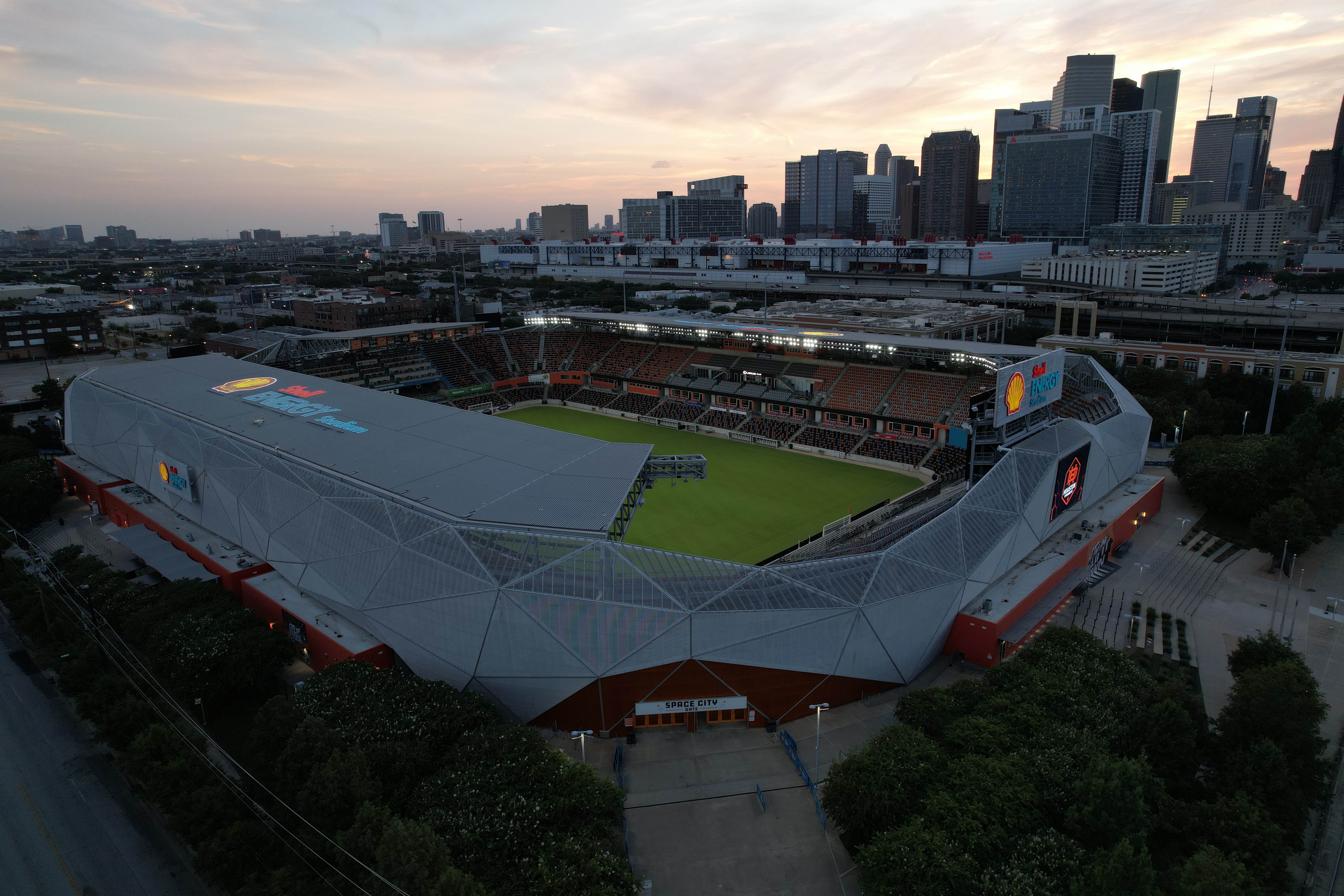 Aerial view of a soccer stadium at dusk with a city skyline behind it.