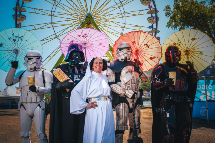 Five people dressed as Star Wars characters pose with colorful parasols in front of a Ferris wheel.