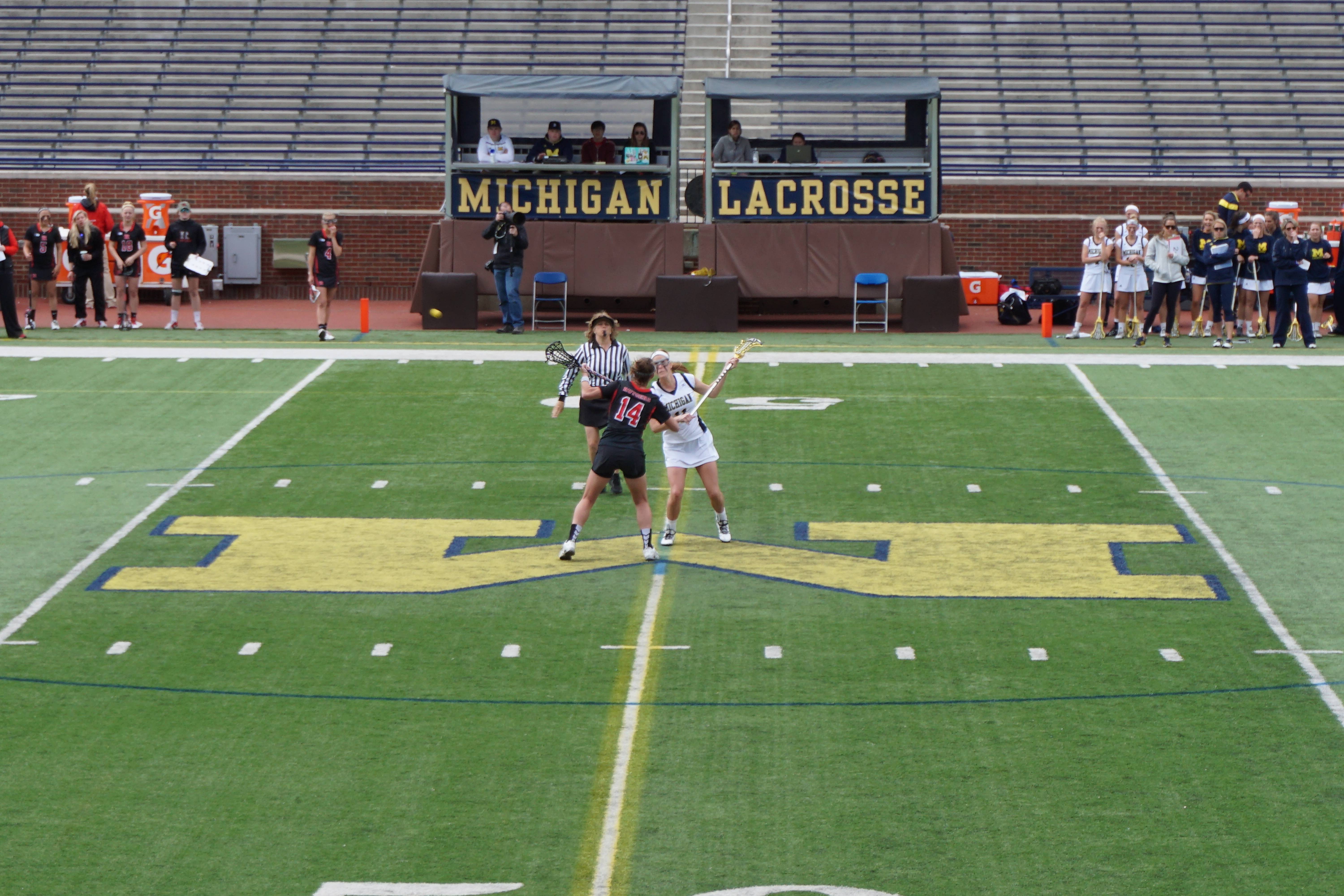 Two women's lacrosse players face off at midfield on a turf field.