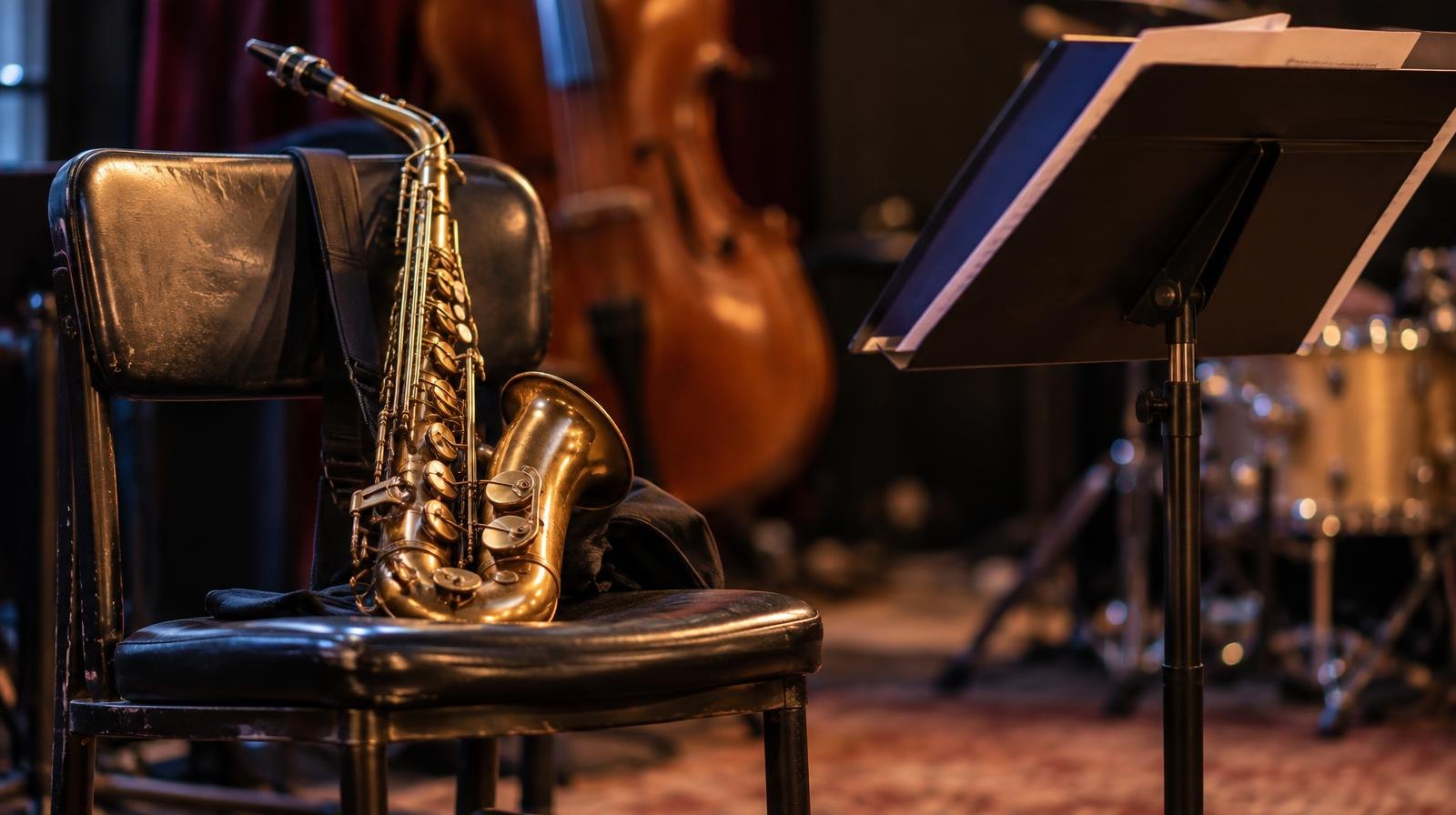 A saxophone resting on a chair next to a music stand on a warmly lit stage.