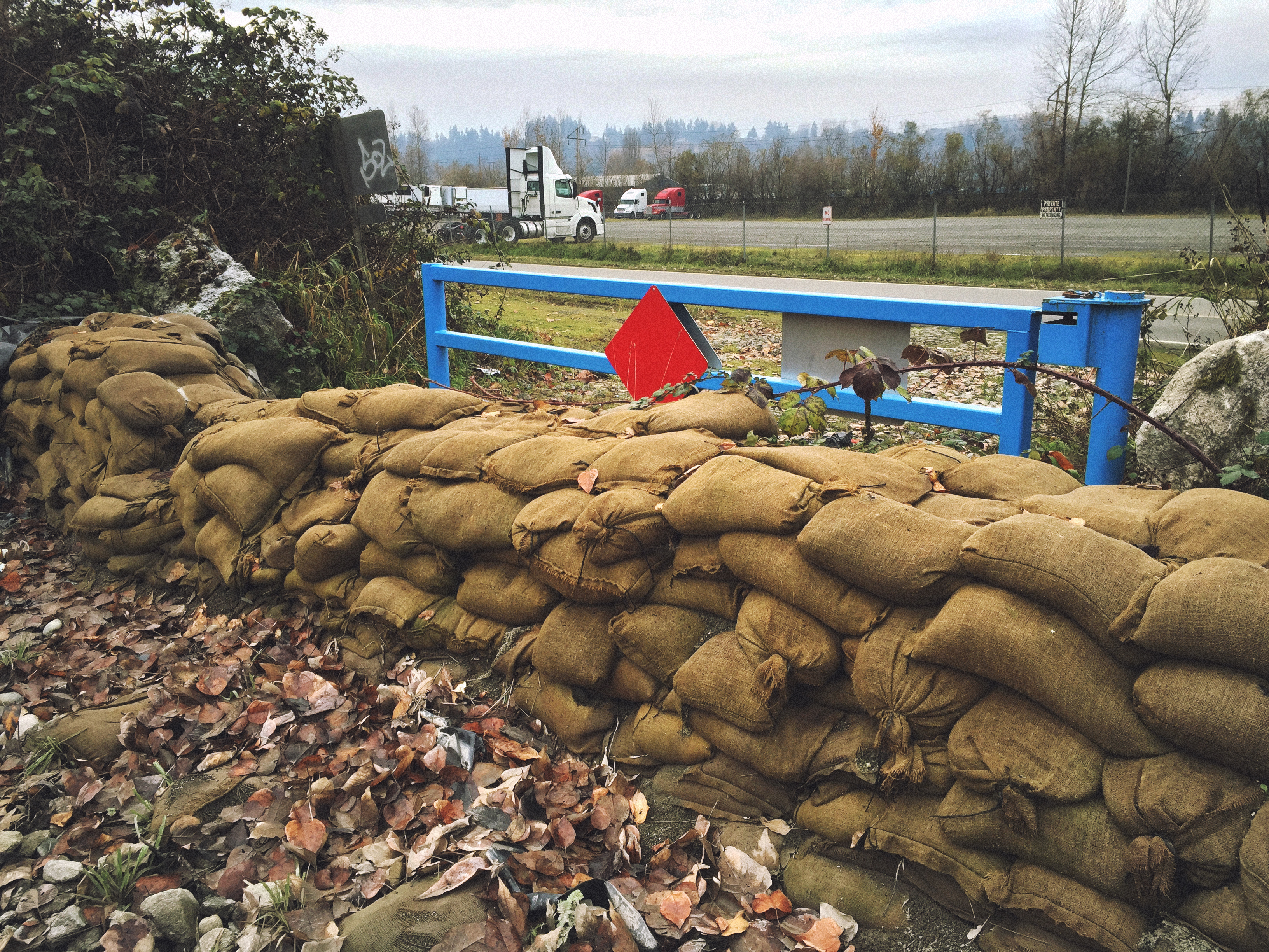 Rows of burlap sandbags stacked as a flood barrier beside a metal railing.
