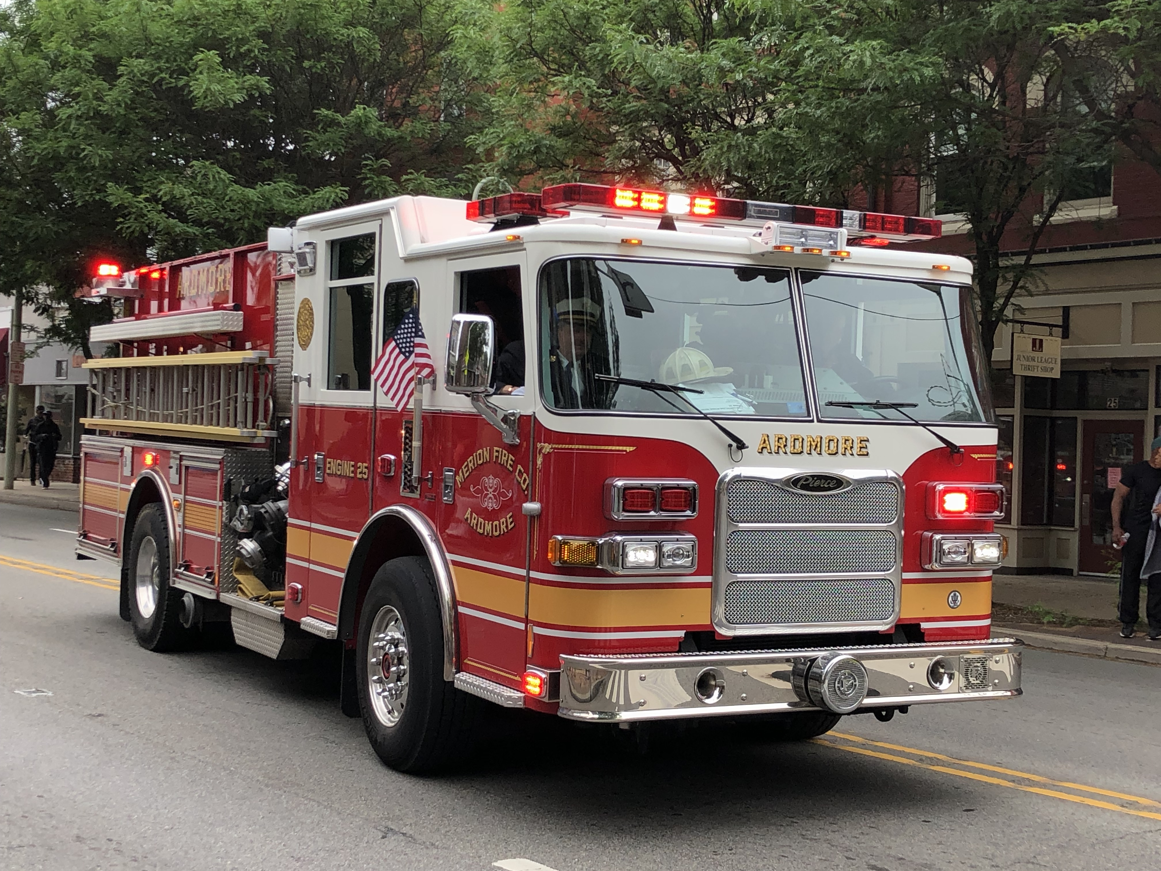 Red fire engine with emergency lights on driving down a tree-lined street.