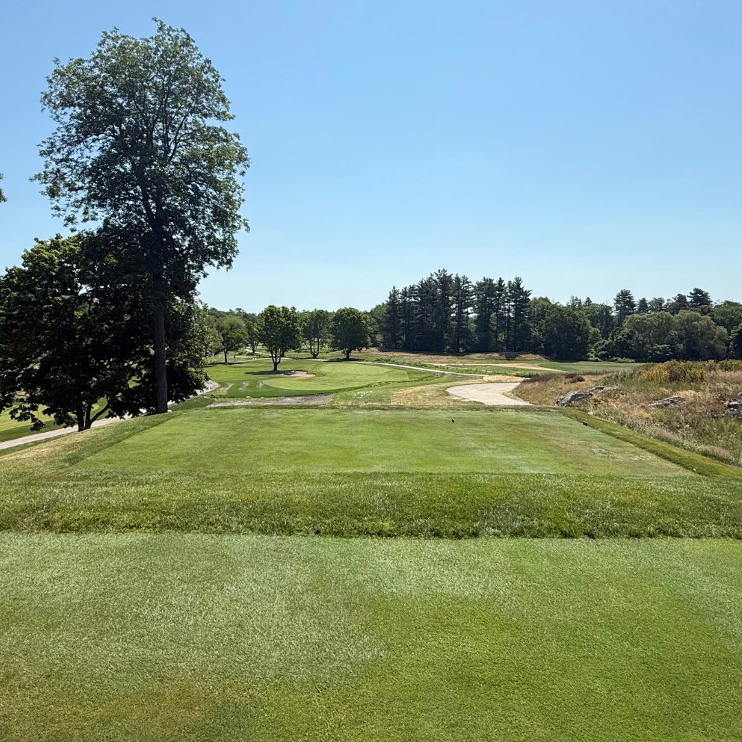 Golf course fairway with sand bunkers, manicured grass, and tree-lined borders under a clear blue sky.