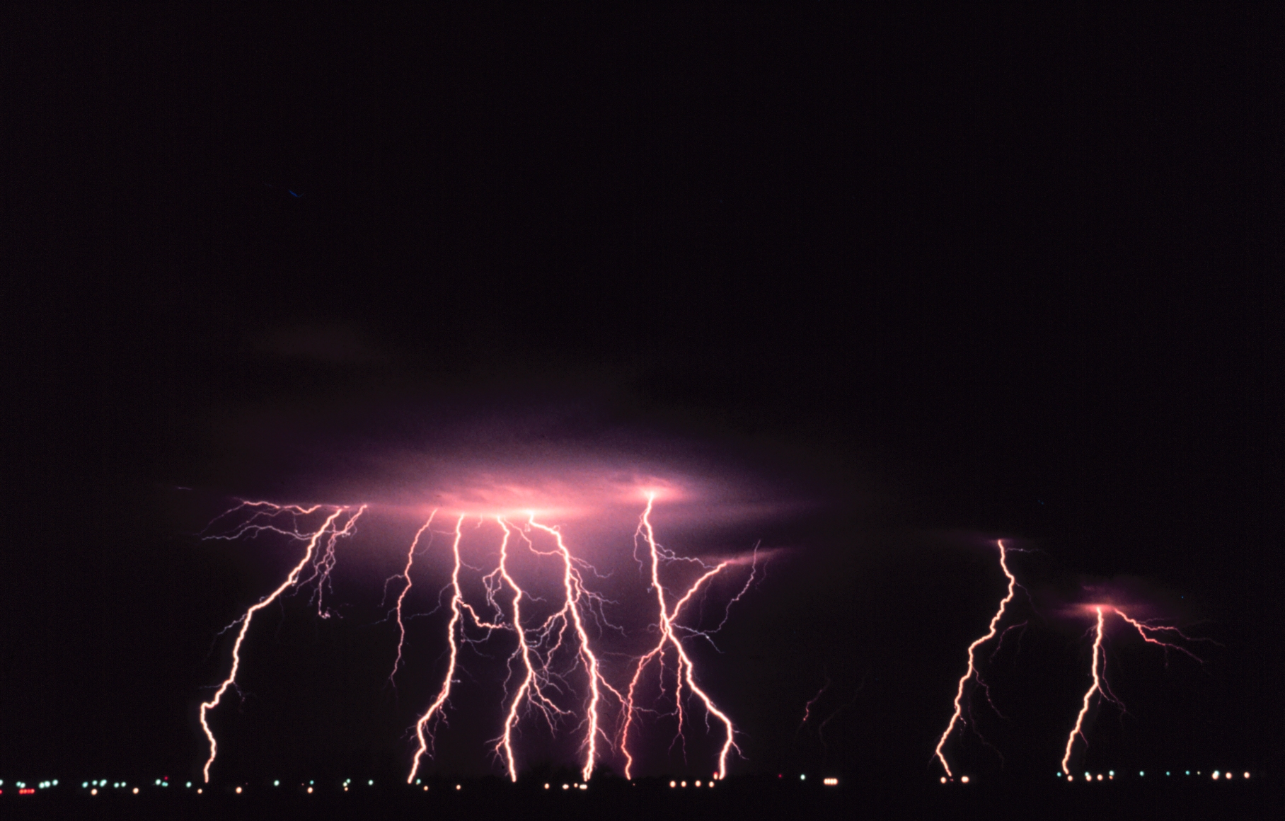 Multiple pink lightning bolts strike downward from a dark night sky.