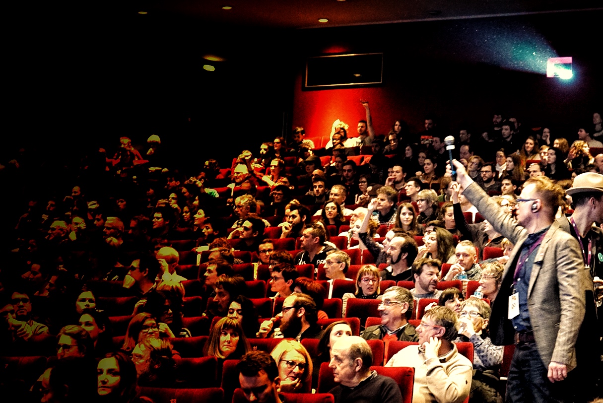 Audience seated in red cinema chairs watching a short film festival screening.