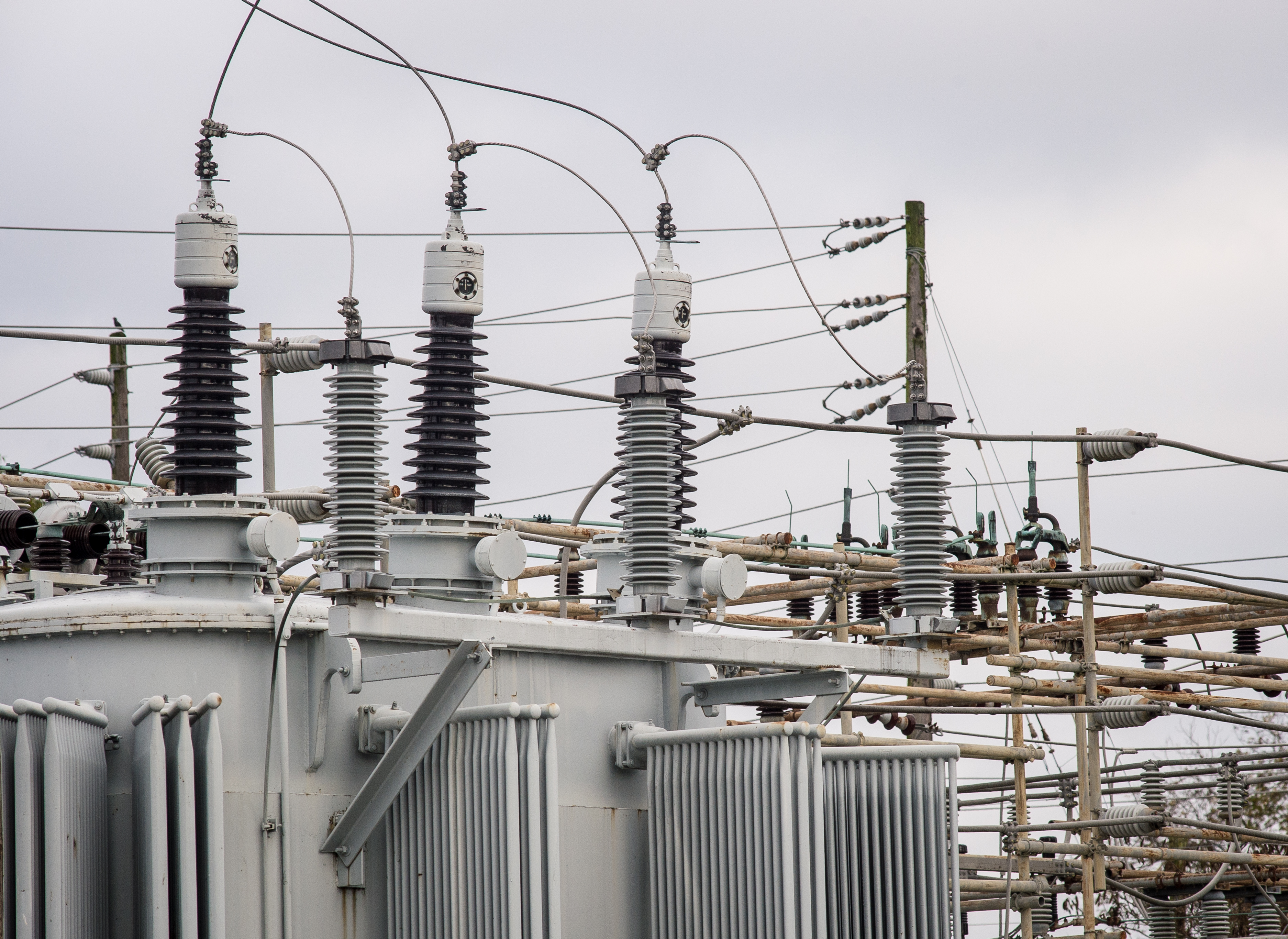 Large power transformers and high-voltage insulators at an electrical substation under an overcast sky.