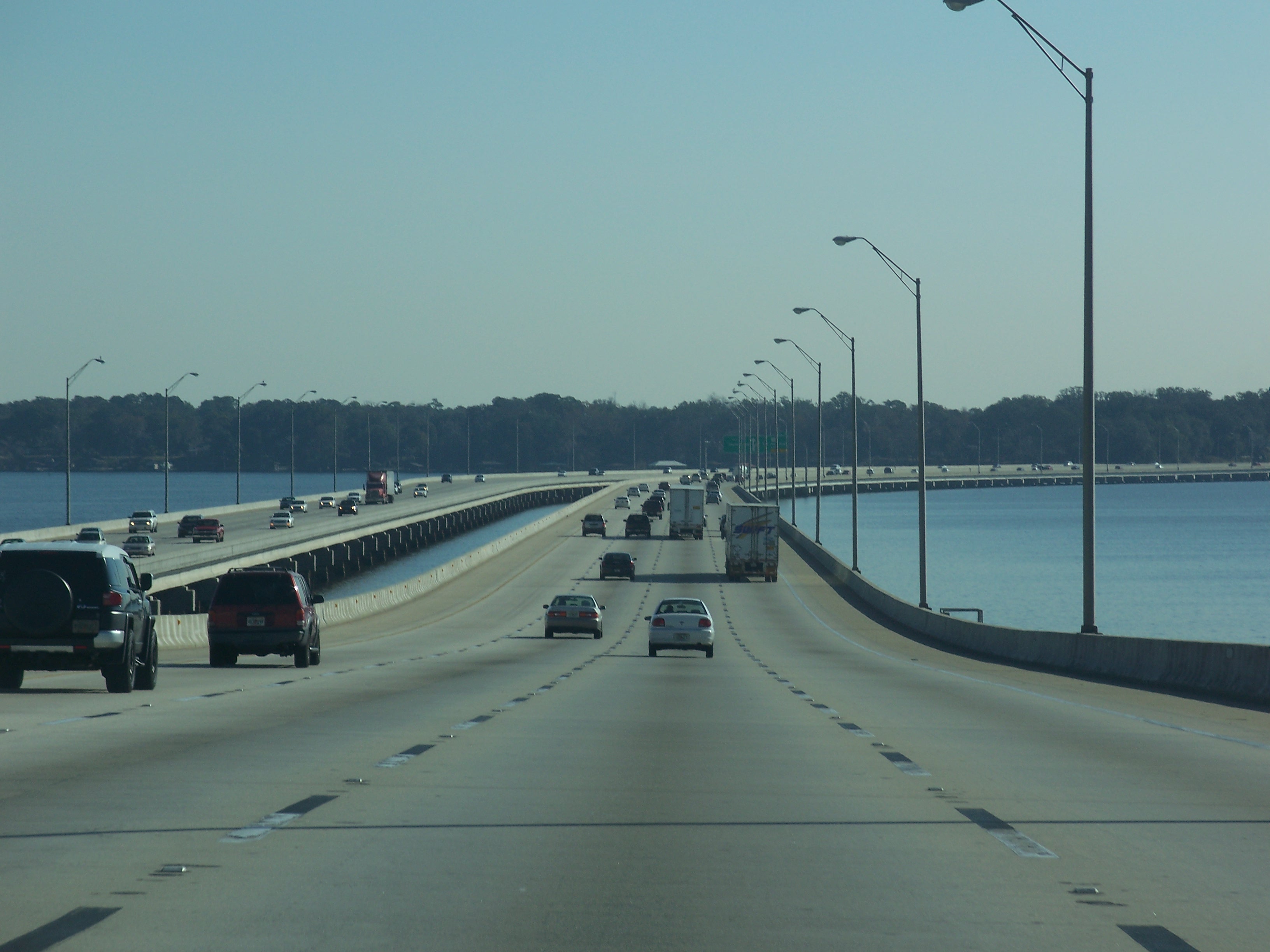 Multi-lane highway bridge over water with vehicles and street lights under a clear sky.