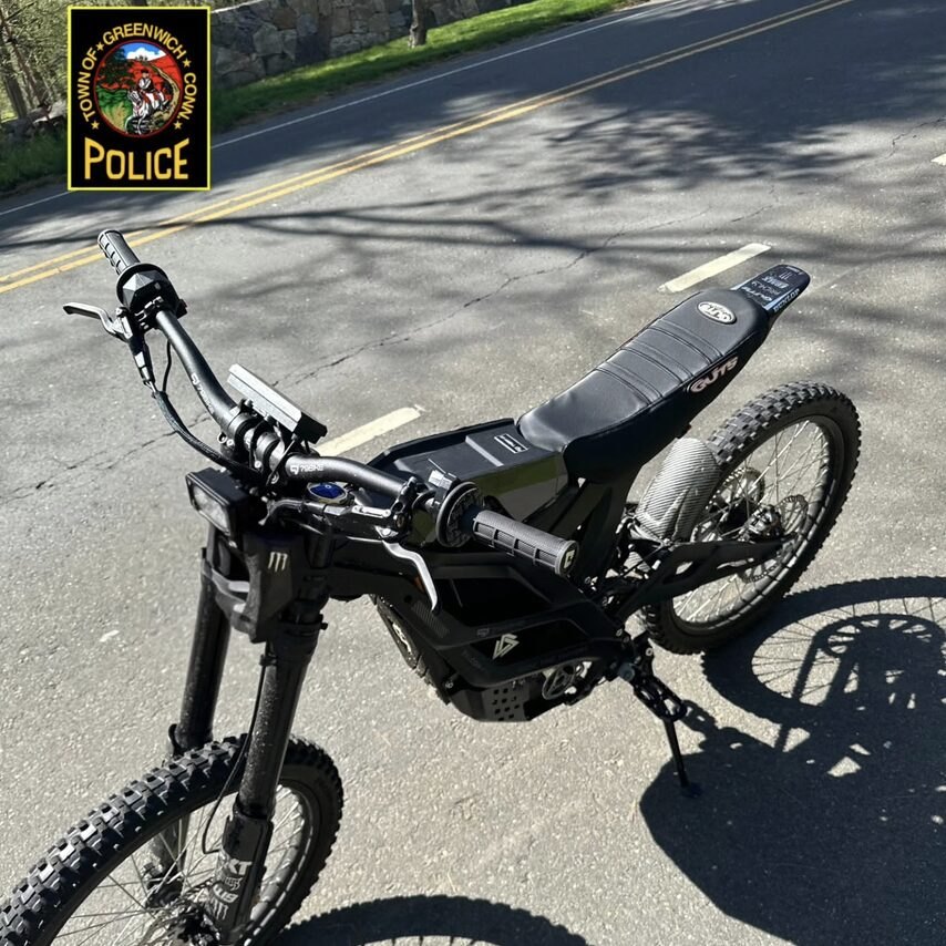Black electric dirt bike with knobby tires parked on pavement, viewed from above.