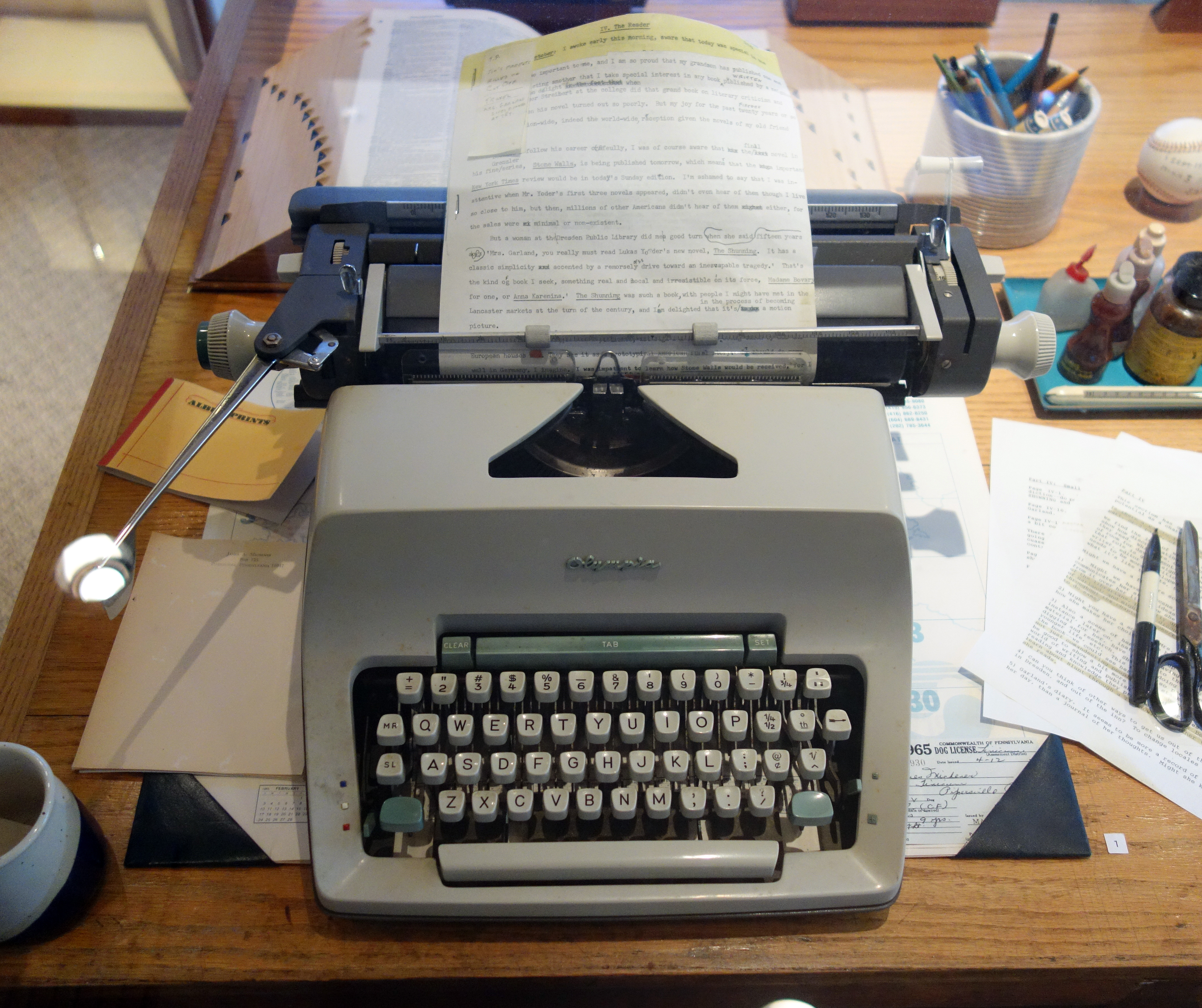 Vintage gray typewriter with a typed page loaded, sitting on a cluttered wooden desk.