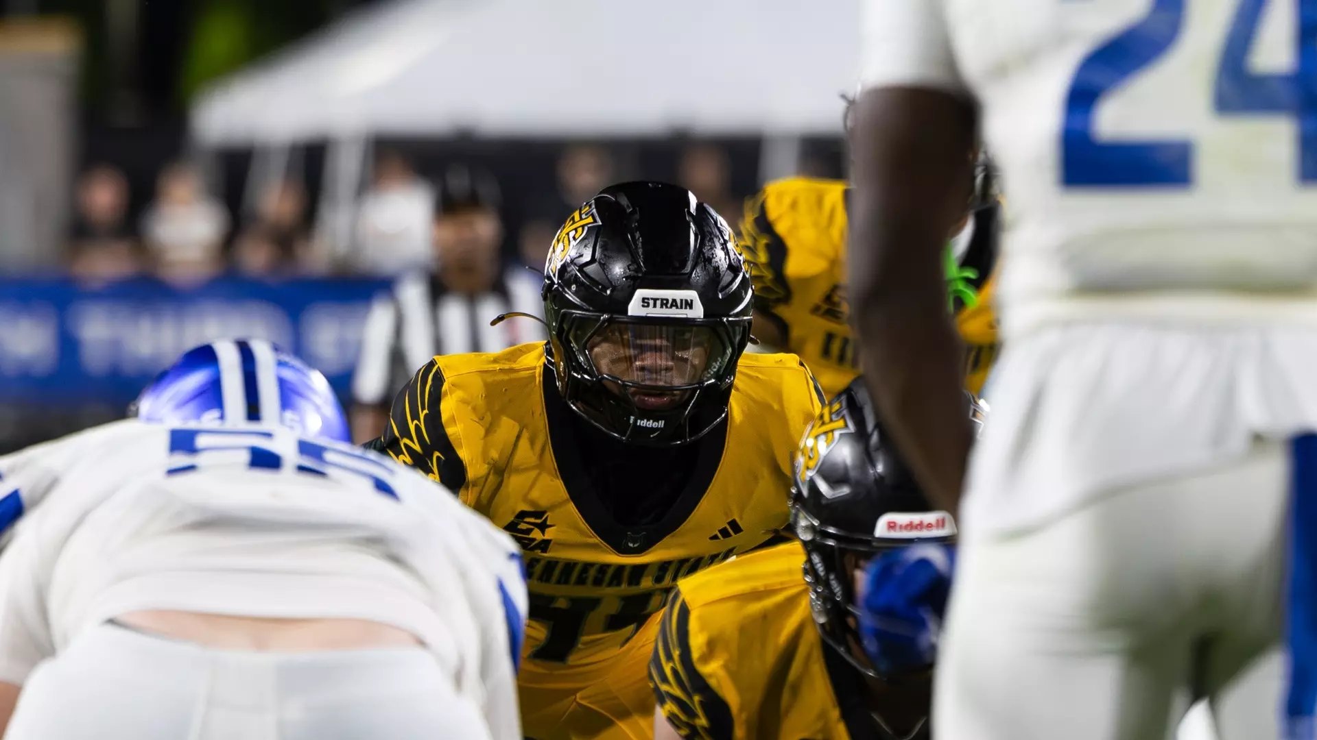 A football player in a gold and black uniform crouched at the line of scrimmage.