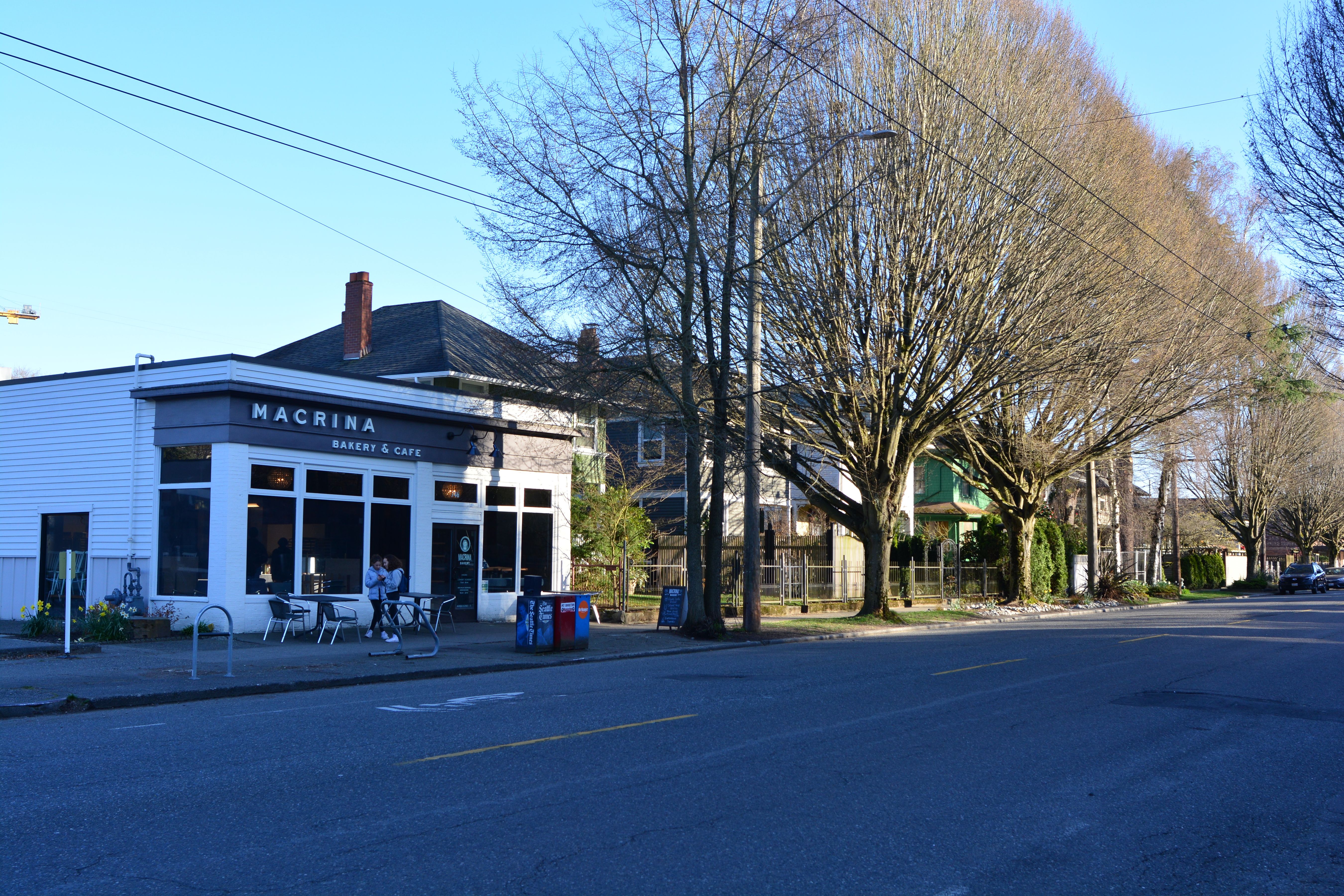 Exterior of a white-sided bakery and café with outdoor seating and bare trees.
