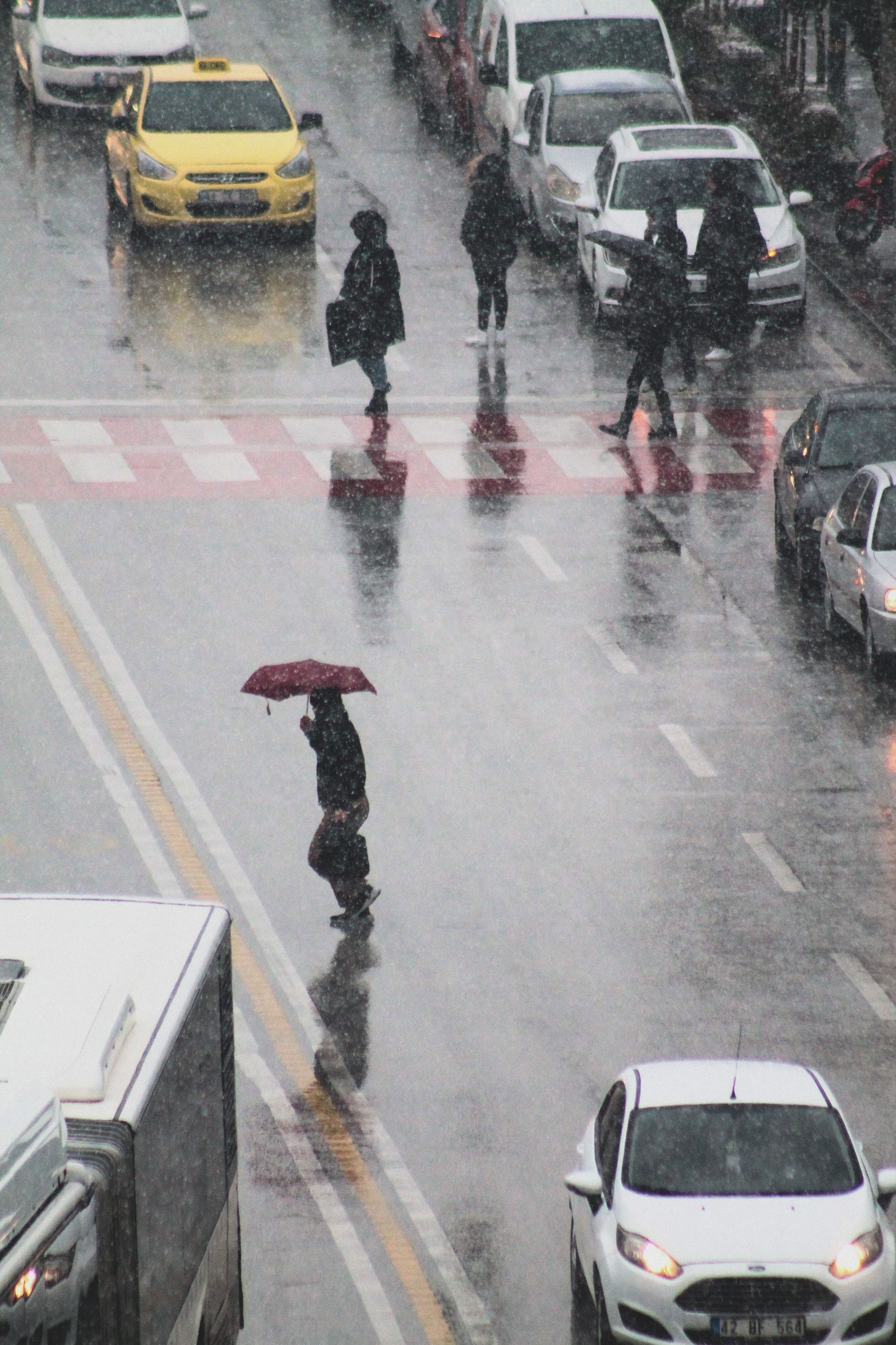 People crossing a busy street in the rain, holding umbrellas and walking amidst traffic.