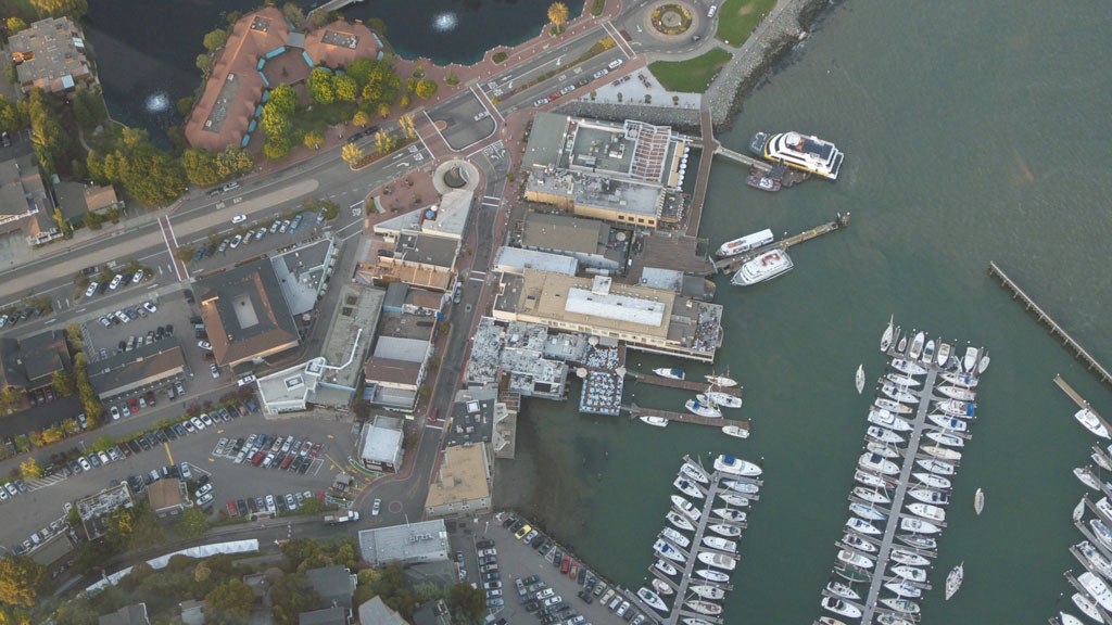 Aerial view of a waterfront town with a marina, commercial buildings, and parking lots along the shoreline.