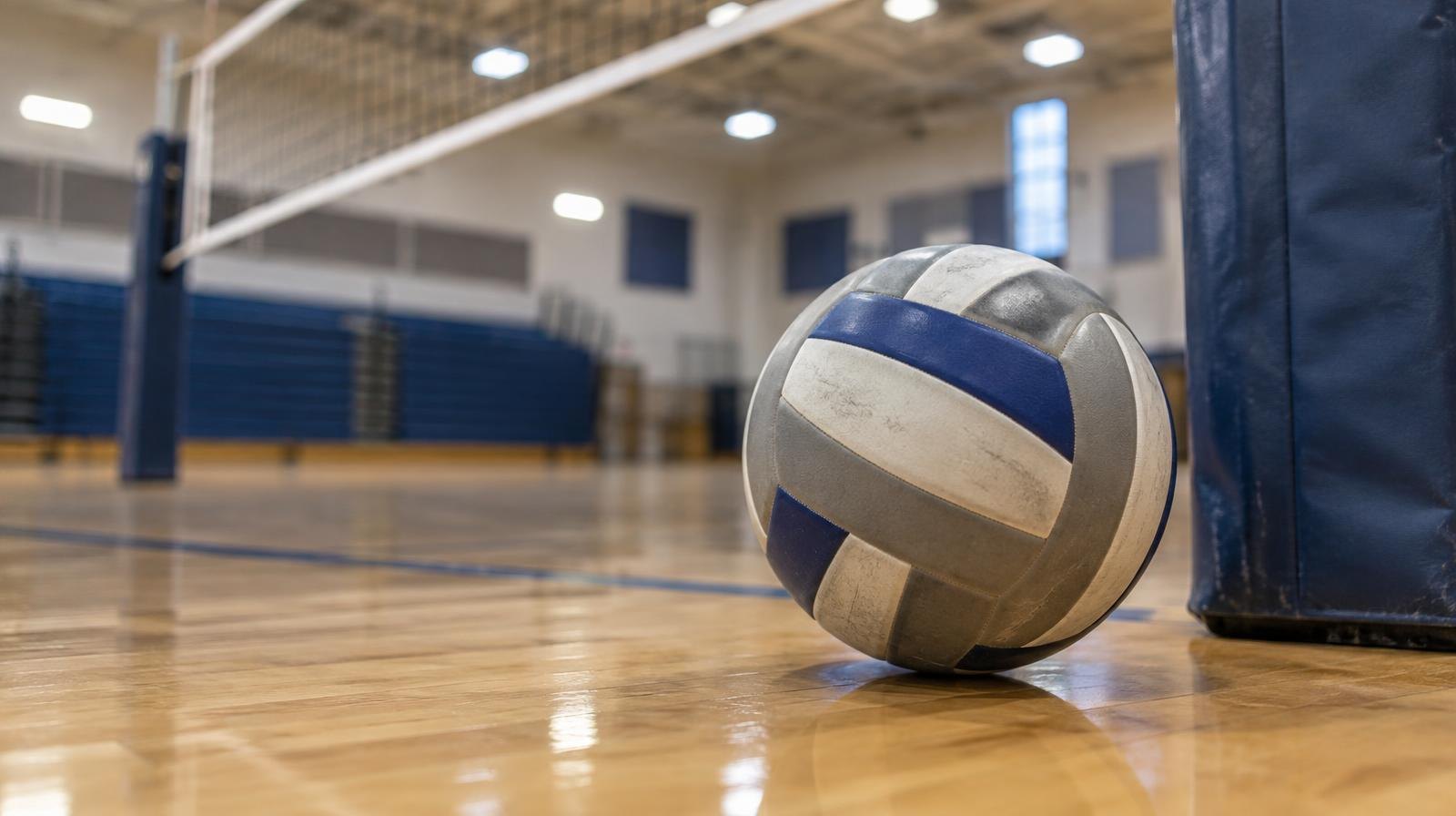 A volleyball resting on a hardwood gymnasium floor near the net post.