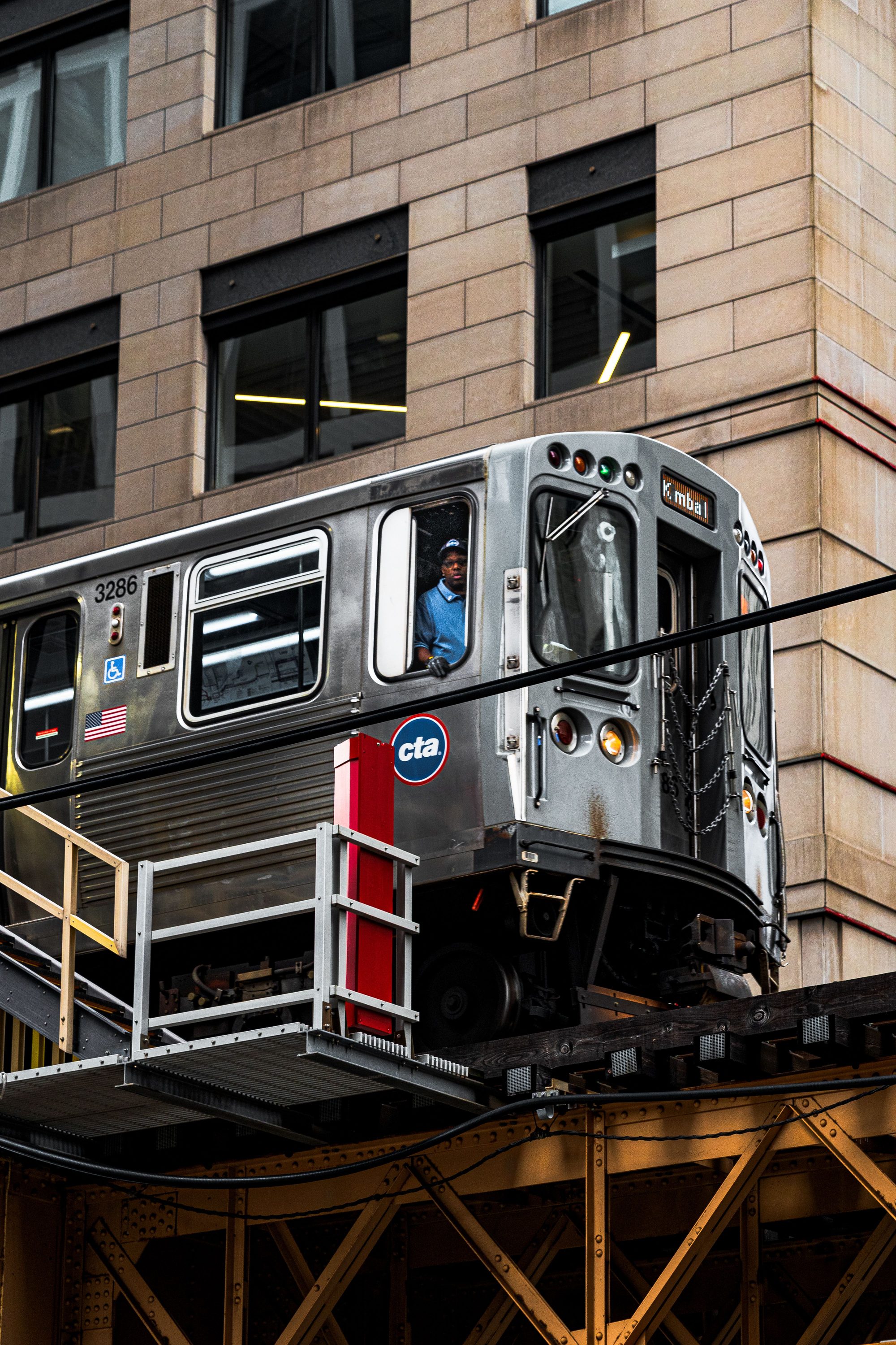 Urban elevated CTA train passing through downtown Chicago with driver in view against modern architecture.