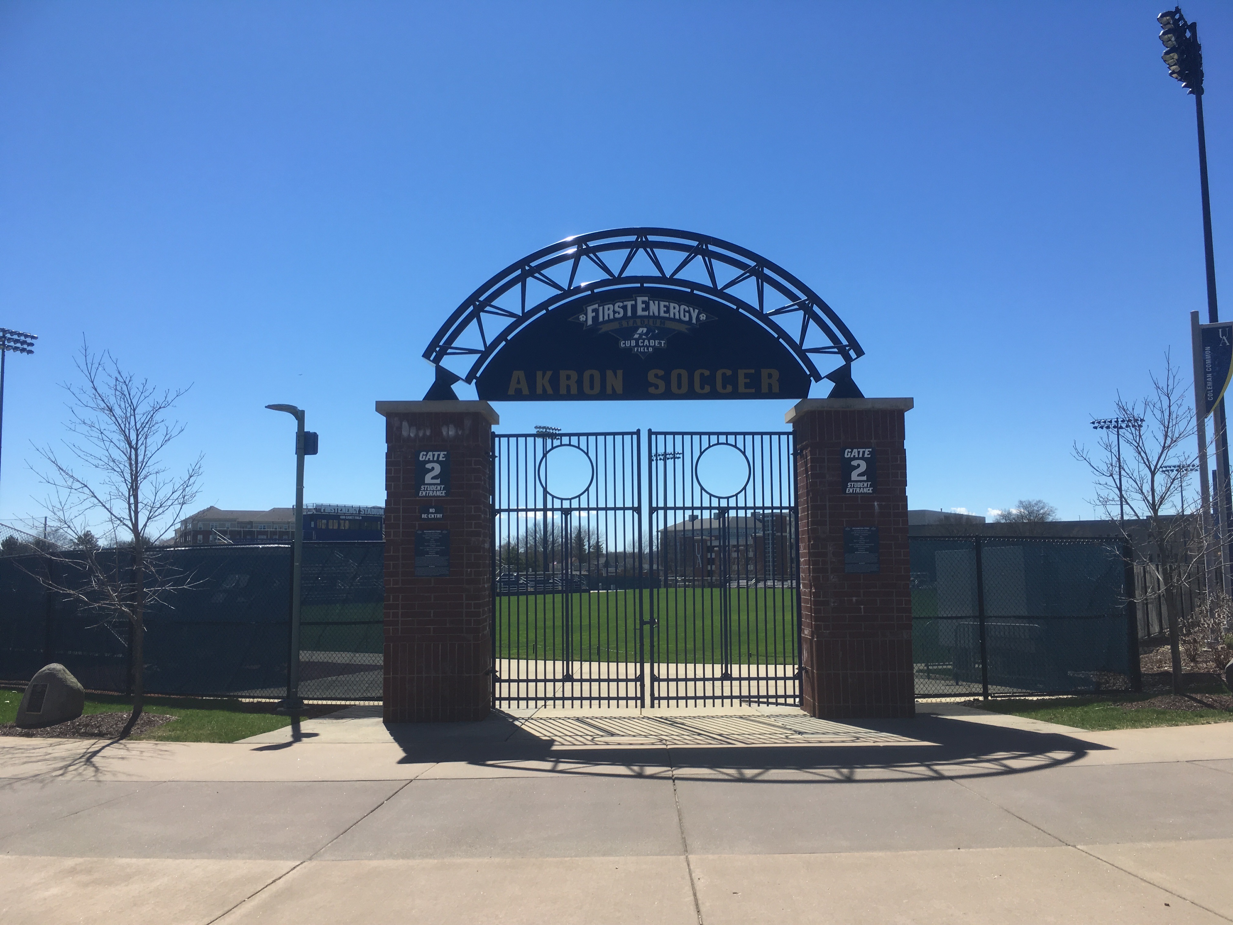 Iron gate entrance with brick pillars and an arched sign reading 'Akron Soccer.'