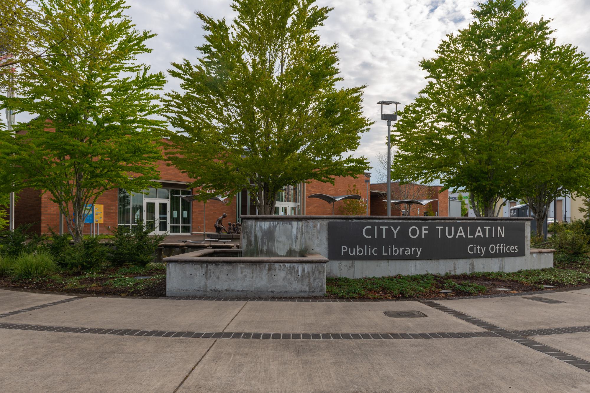 Stone monument sign for Tualatin City Hall and Public Library in front of a red brick building.