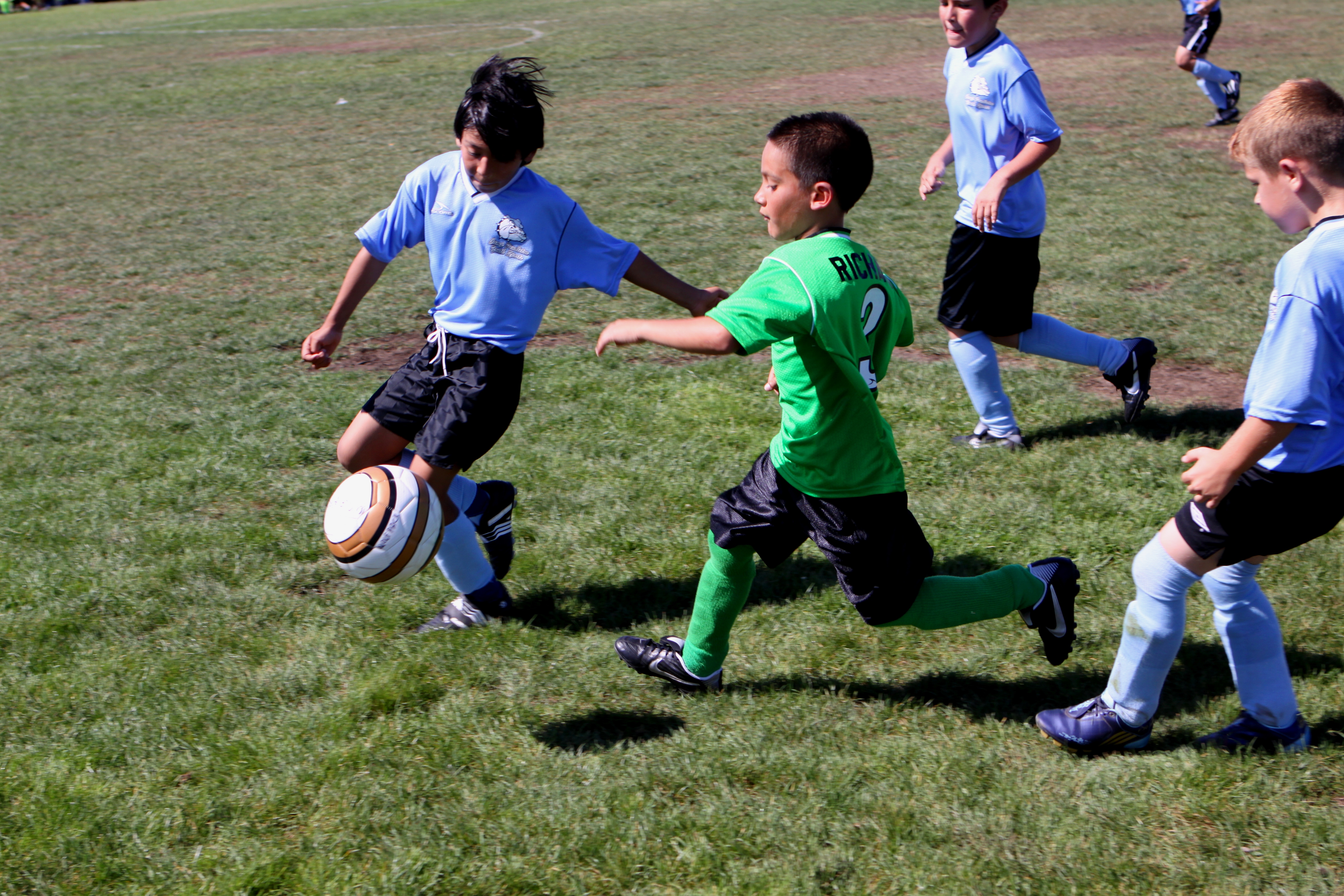Young boys in soccer uniforms competing for a ball on a grass field.