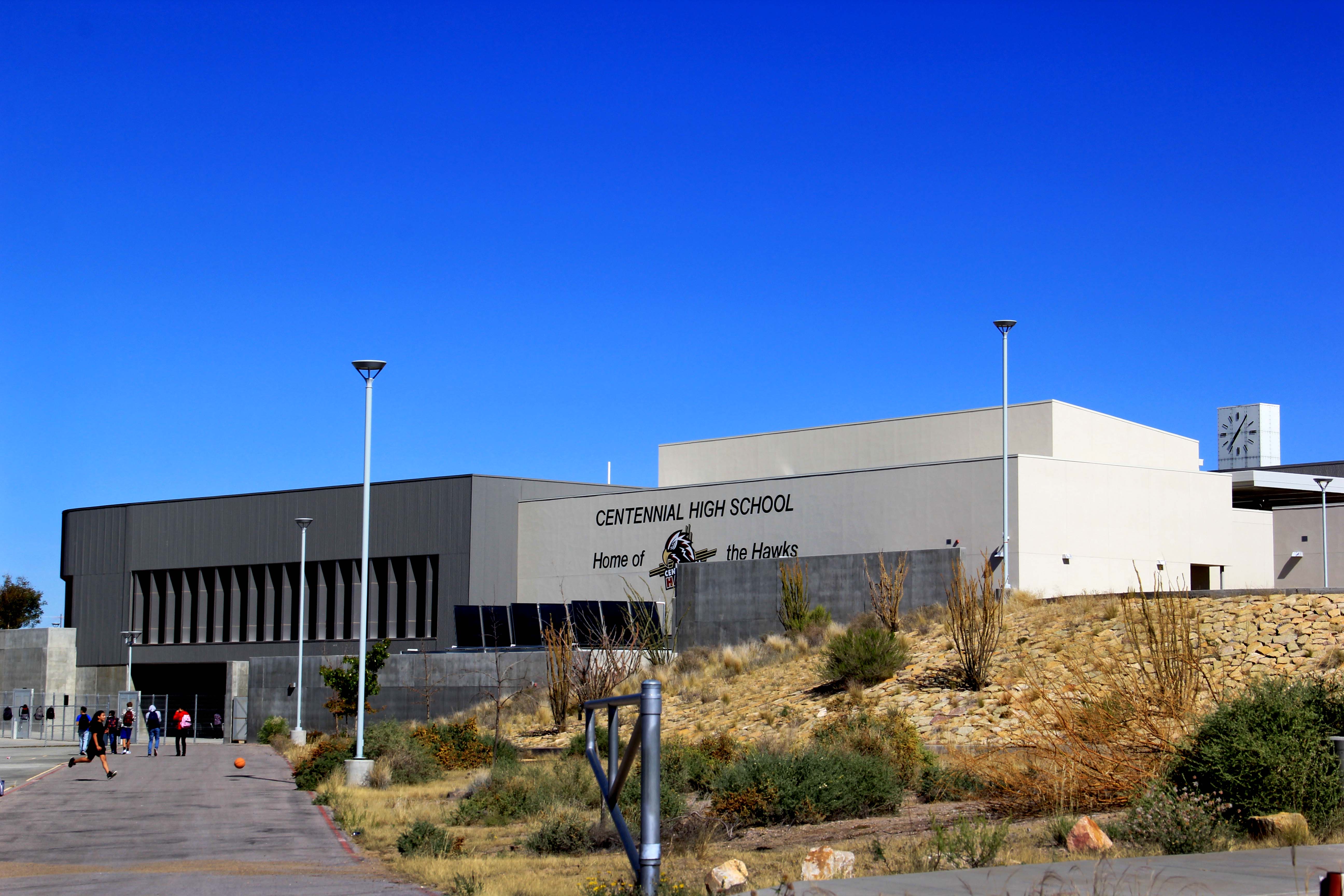 Exterior of a high school building with a clock tower and desert landscaping under a clear blue sky.