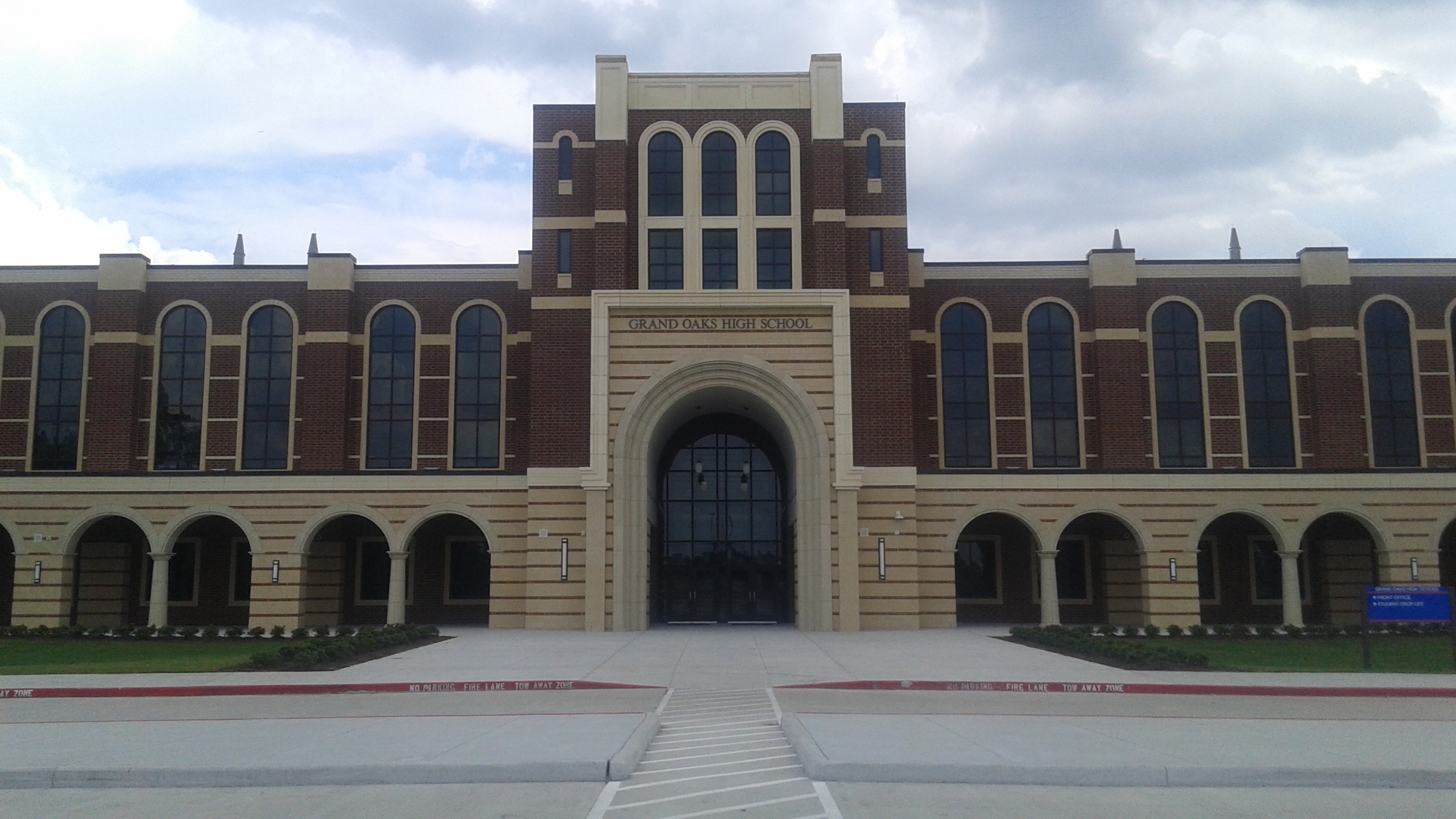 Brick high school building with arched entrance and central tower viewed from the front walkway.