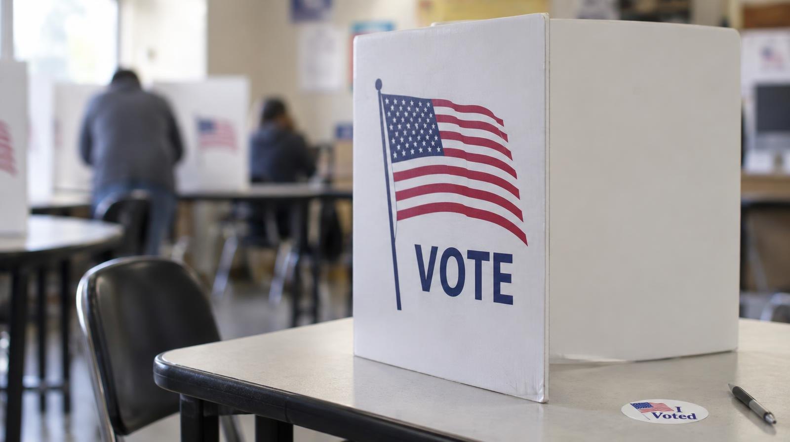 A portable voting booth on a table under fluorescent lighting.