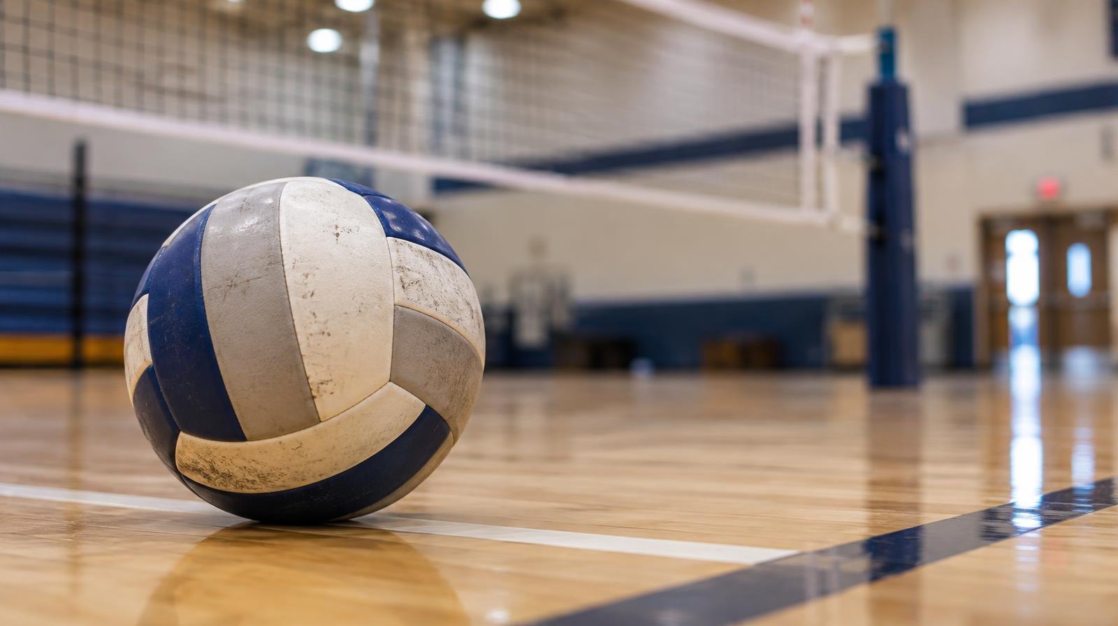 A volleyball resting on a hardwood gym floor near the net.