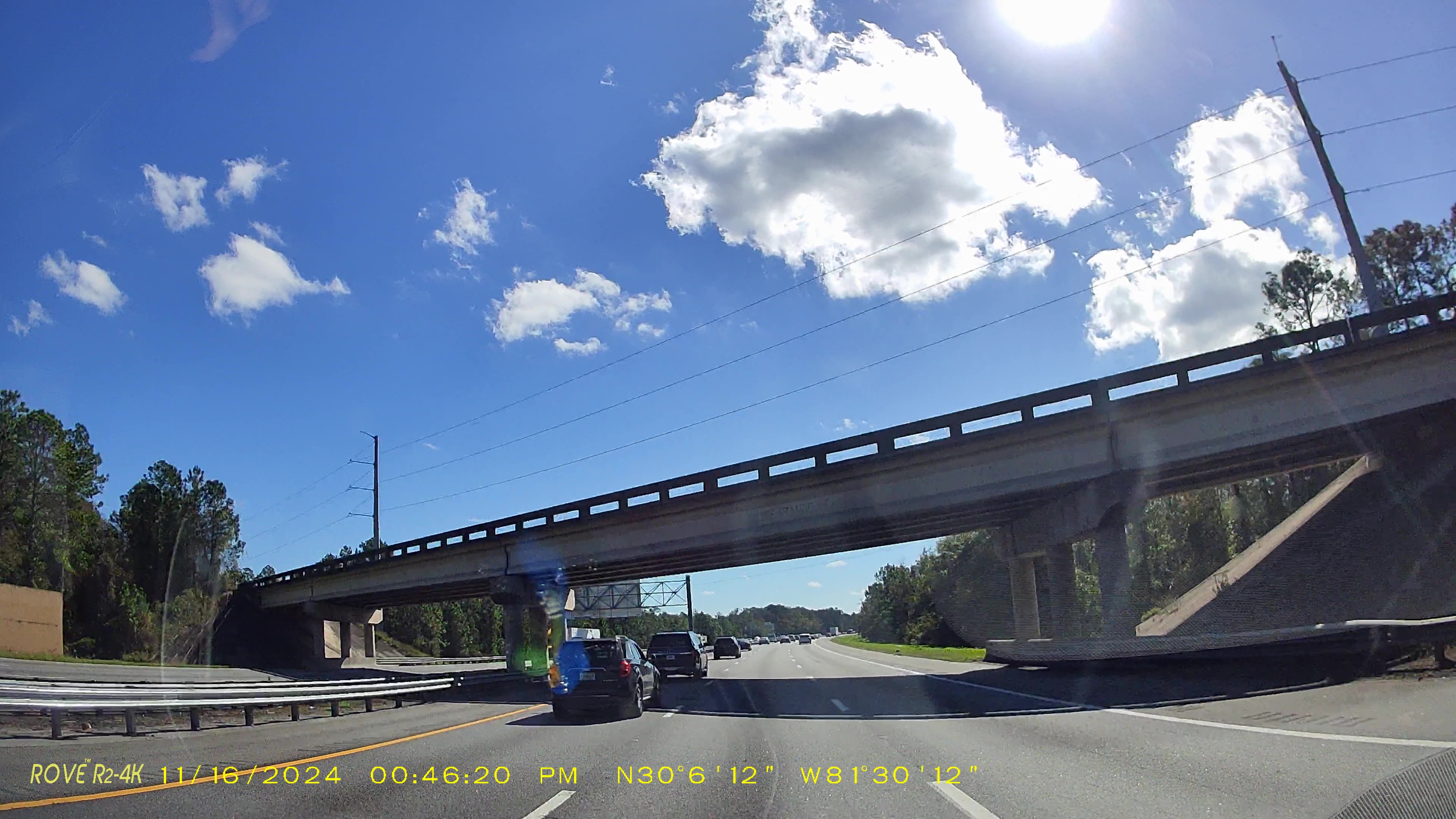 Overpass bridge spanning a multi-lane highway with vehicles below and trees on both sides.
