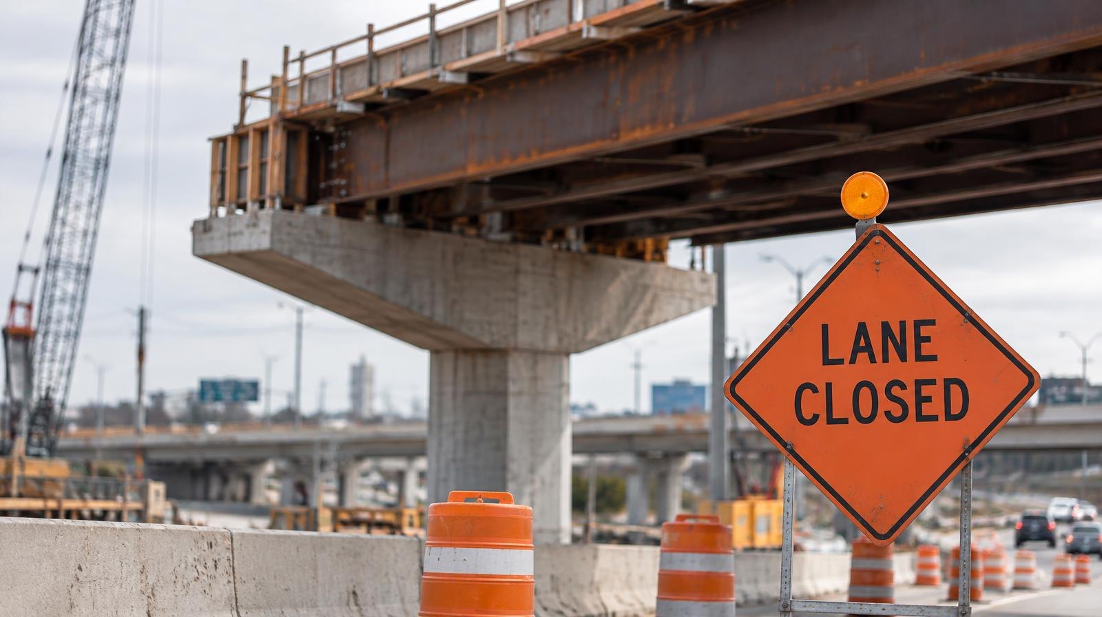 Highway overpass bridge under construction with steel girders and orange traffic cones.