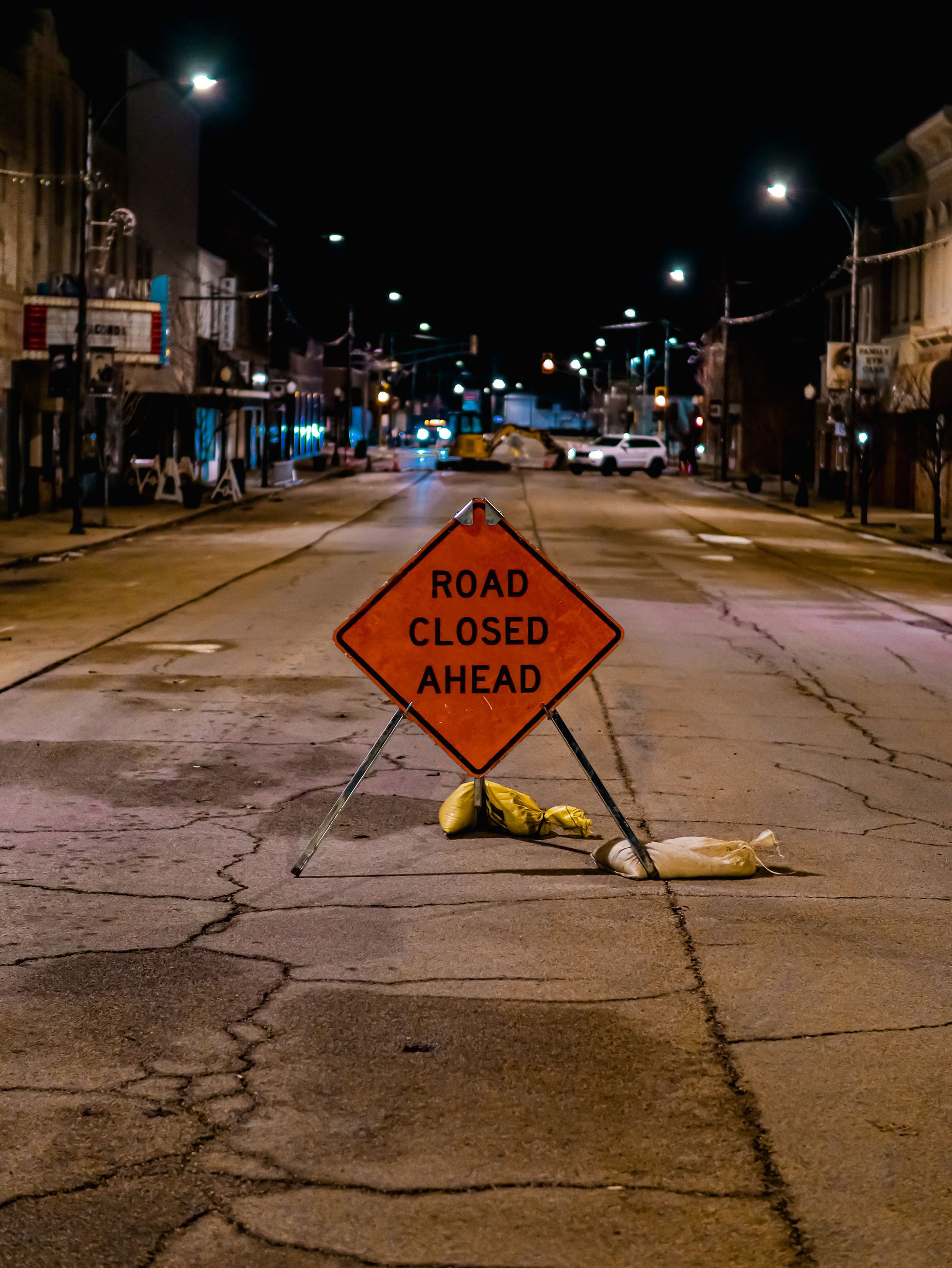 Nighttime street with a road closed sign warns of closure ahead.